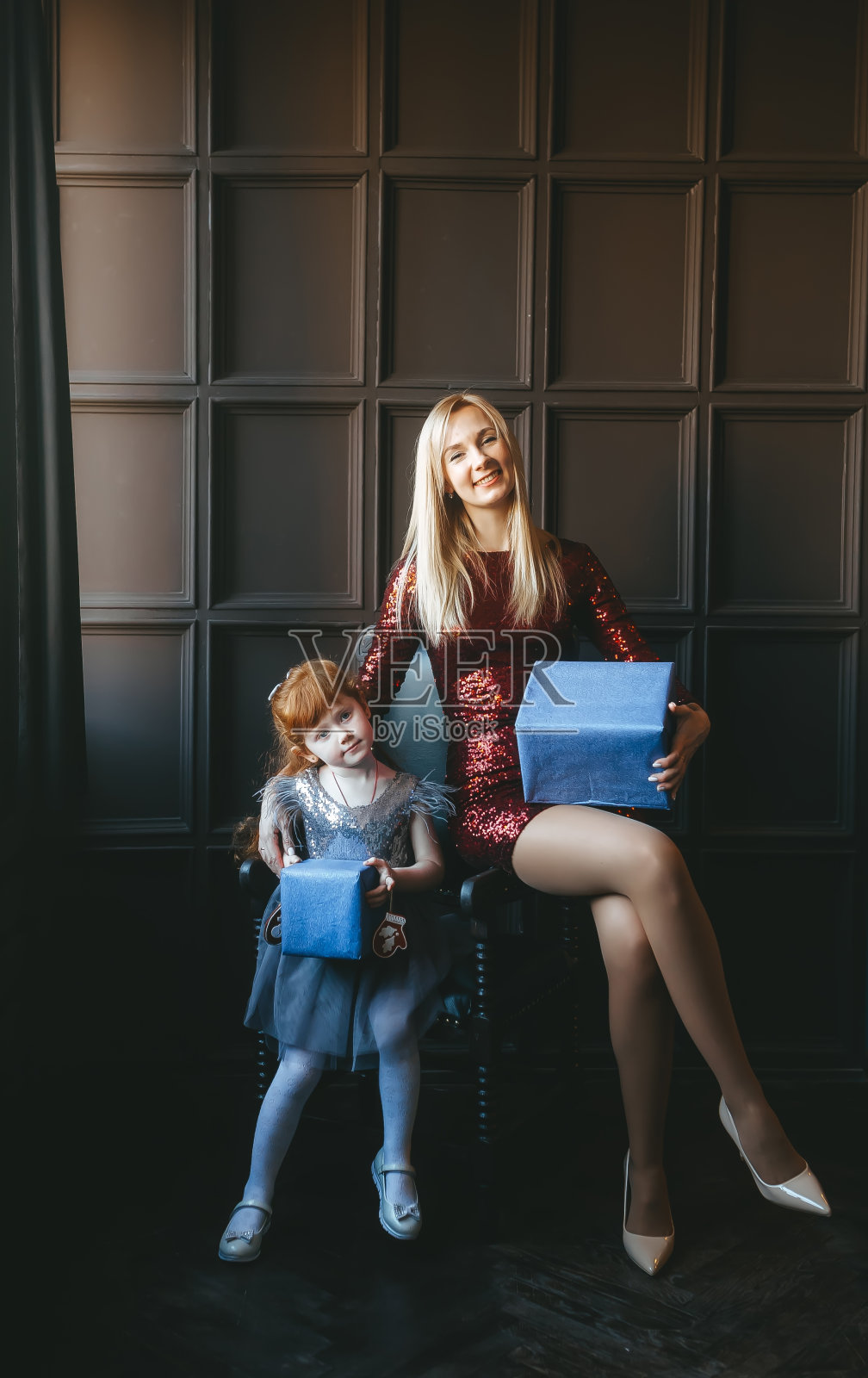 快乐的母亲和她的女儿与礼物盒坐在扶手椅上照片摄影图片