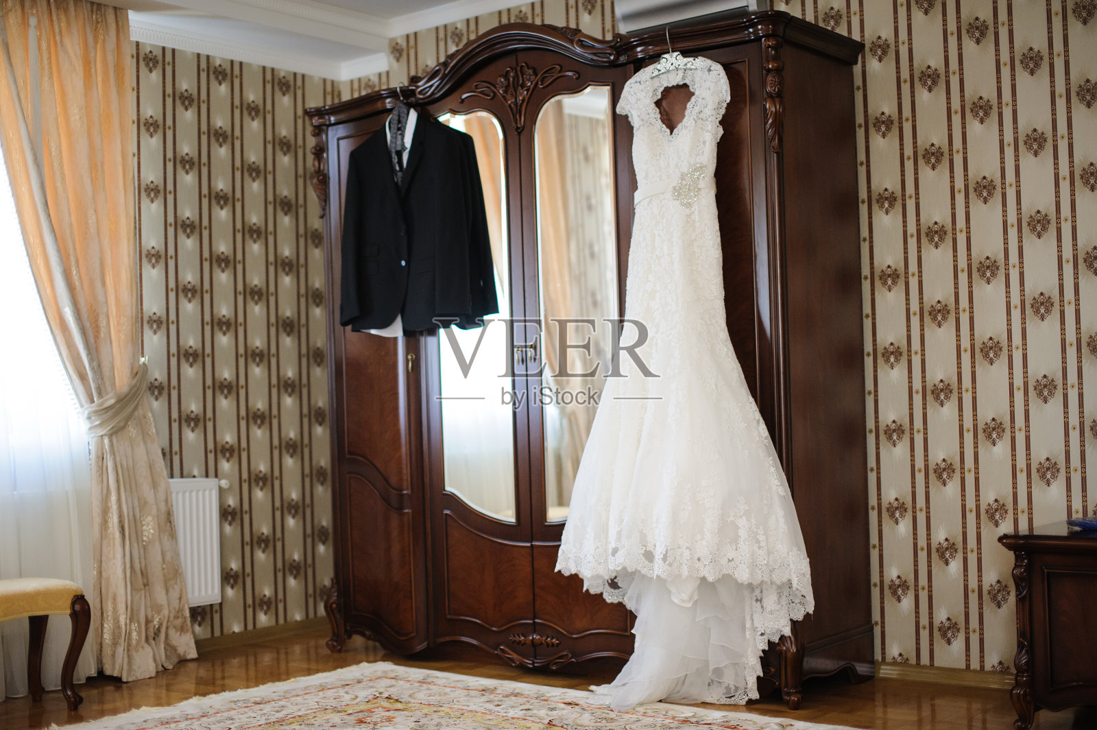美丽优雅的白色婚纱和男新郎的婚礼套间挂在衣柜里，期待着婚礼的到来。照片摄影图片