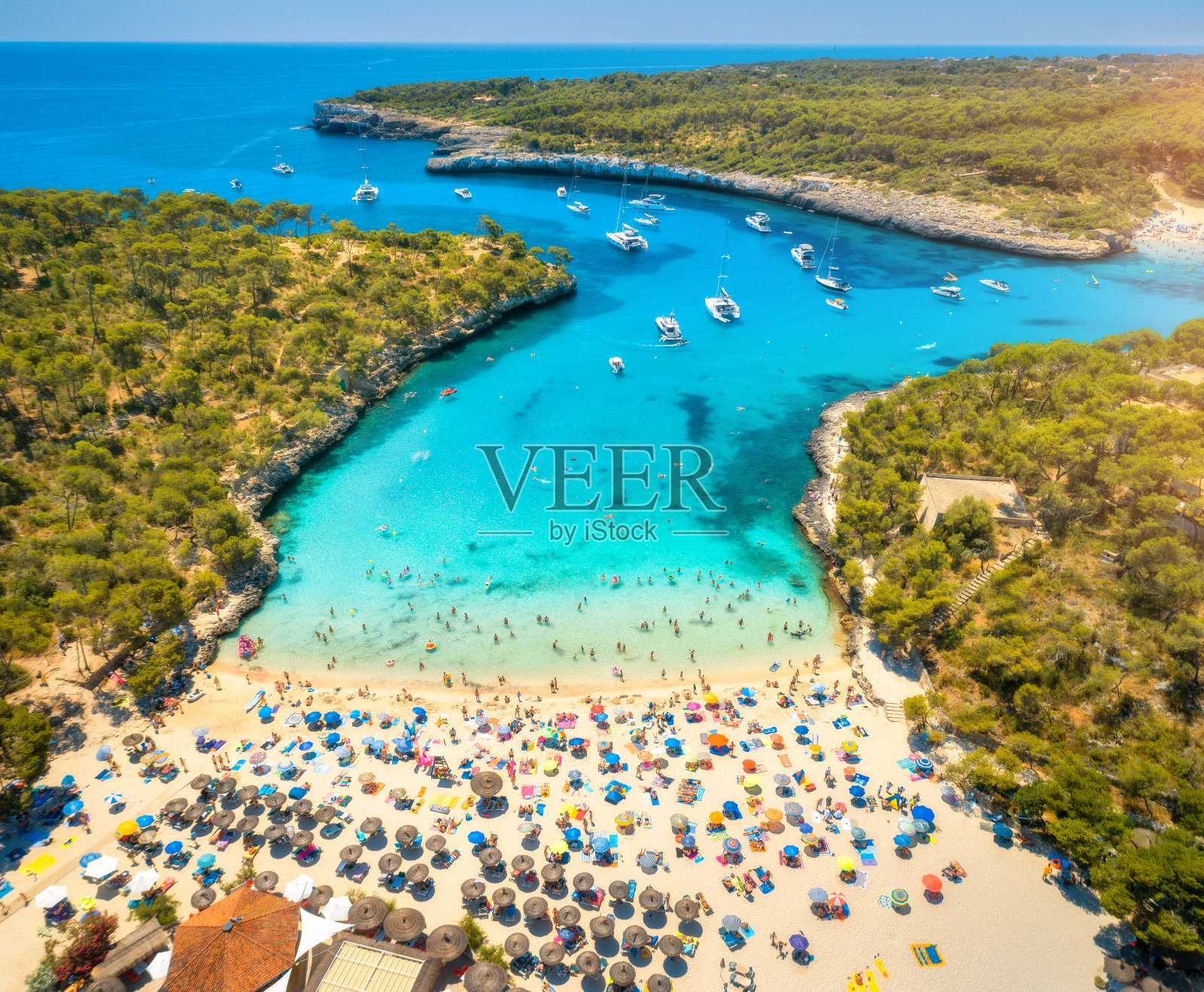 鸟瞰图的沙滩与五颜六色的伞，游泳的人，船和游艇在海湾，绿色的树木和蓝色的水在夏季日落。旅行。巴利阿里群岛,西班牙。前视图。景观照片摄影图片