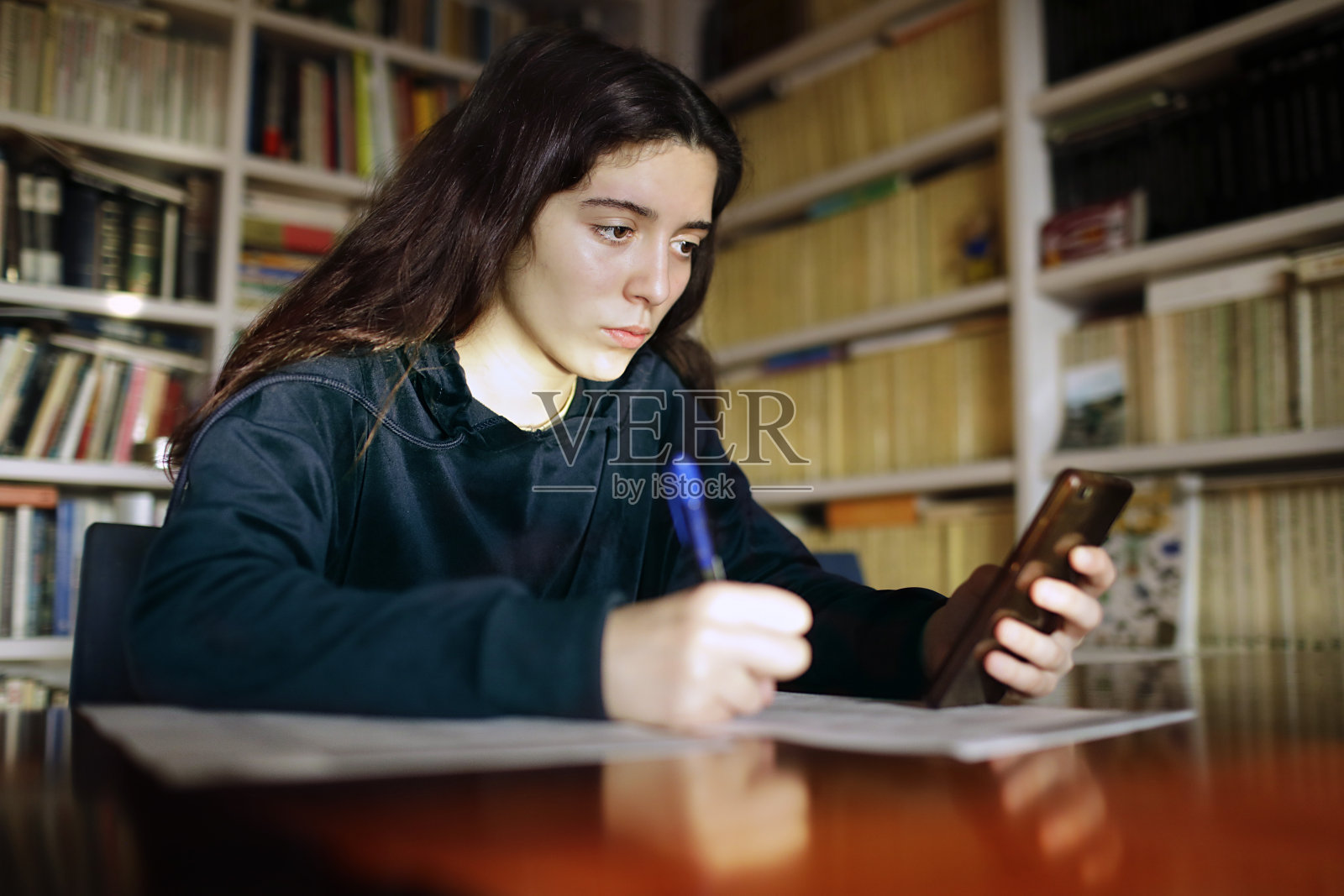一个十几岁的女孩在图书馆里用手机学习照片摄影图片