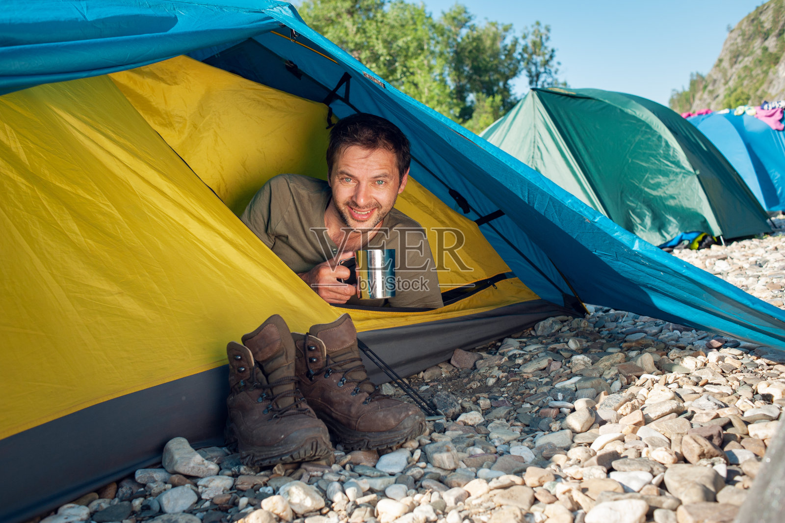 男游客遇到晴朗的早晨，坐在旅游帐篷里，喝着热茶。活动度假概念形象照片摄影图片