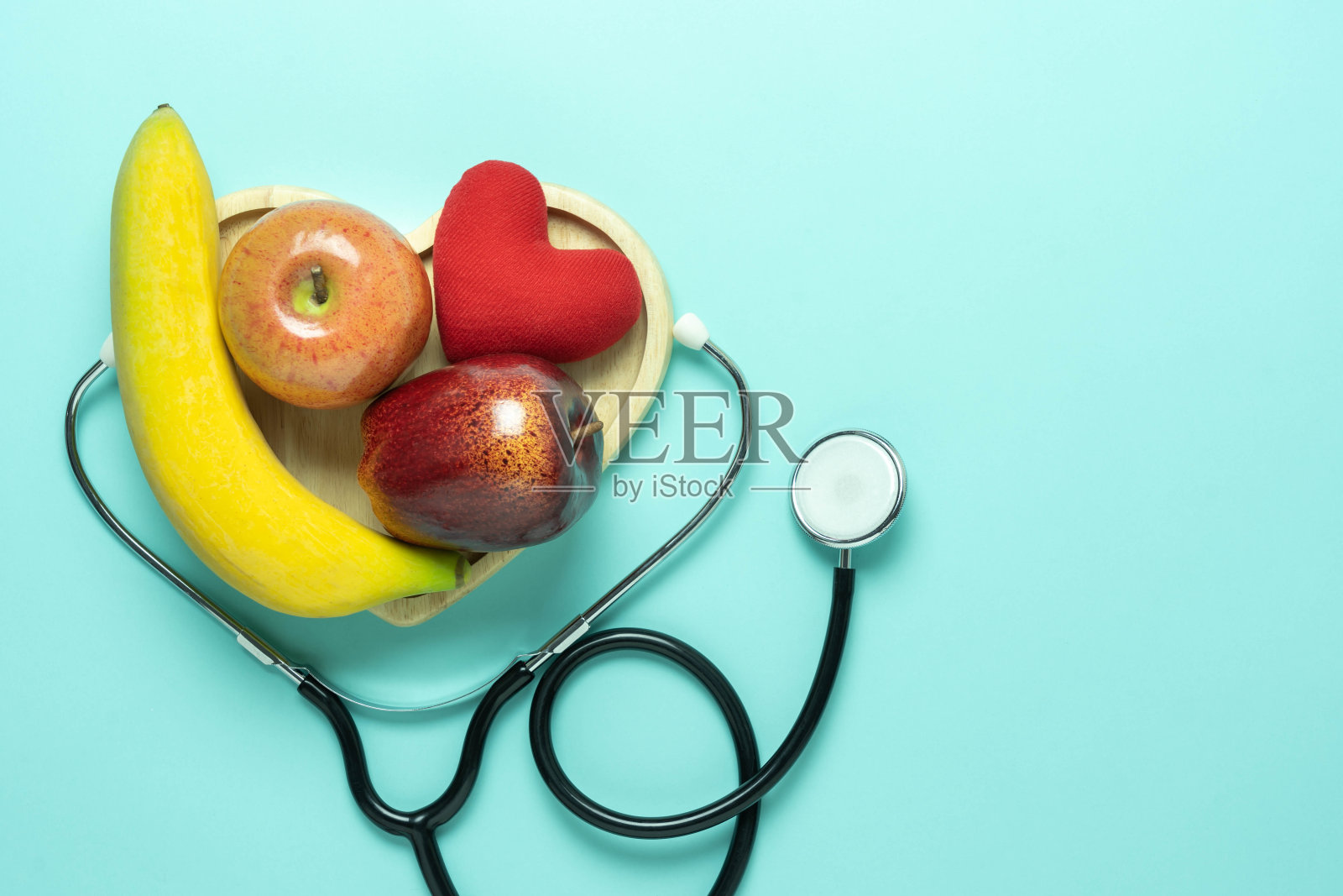 以水果为背景的国家世界卫生日配件保健和医疗的俯视图鸟瞰图。听诊器上有香蕉，苹果，蓝色纸上有红色的心形。本空间照片摄影图片