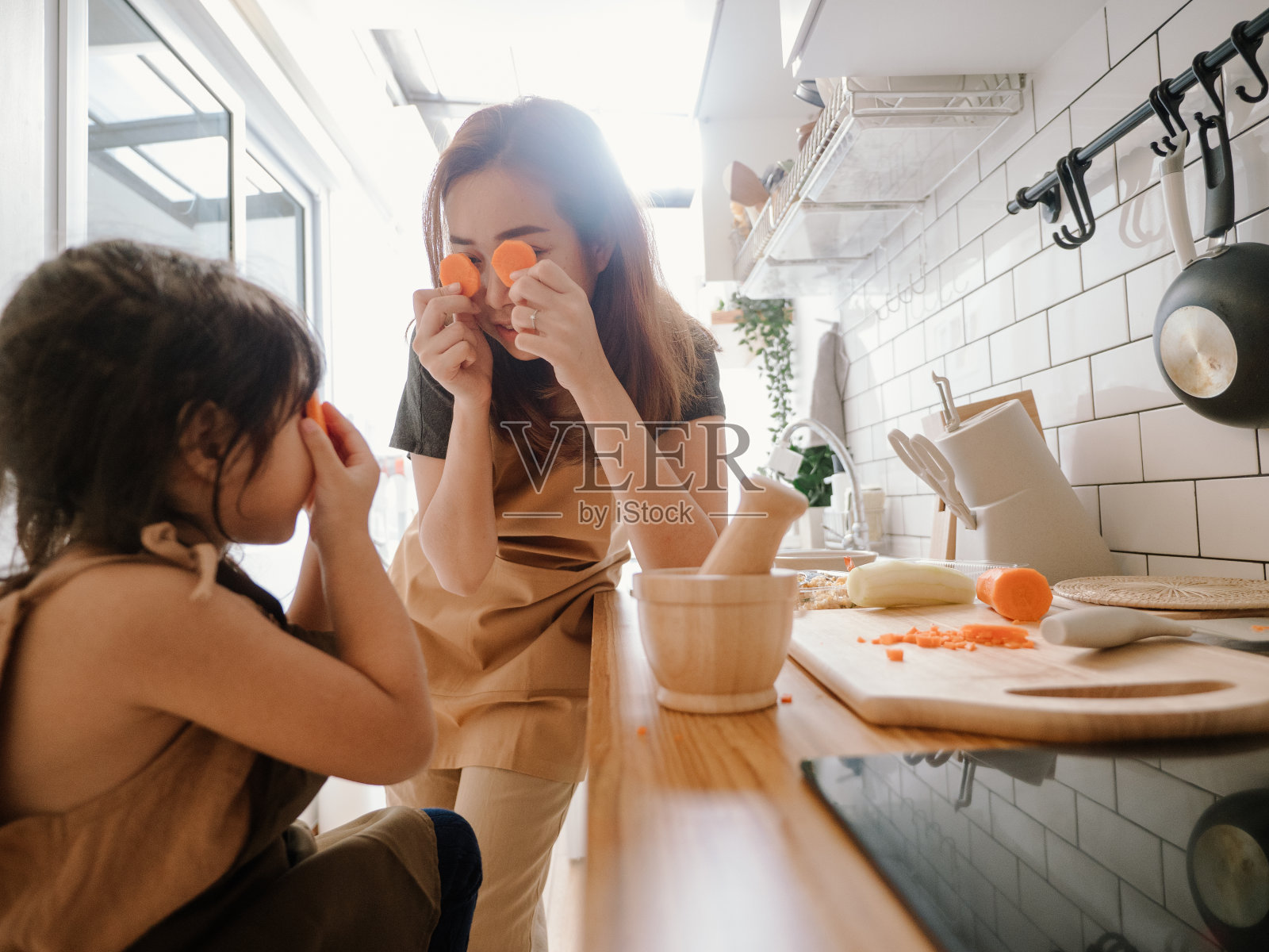 千禧妈妈在厨房准备早餐，而她的女儿在家里帮忙做煎蛋卷。照片摄影图片