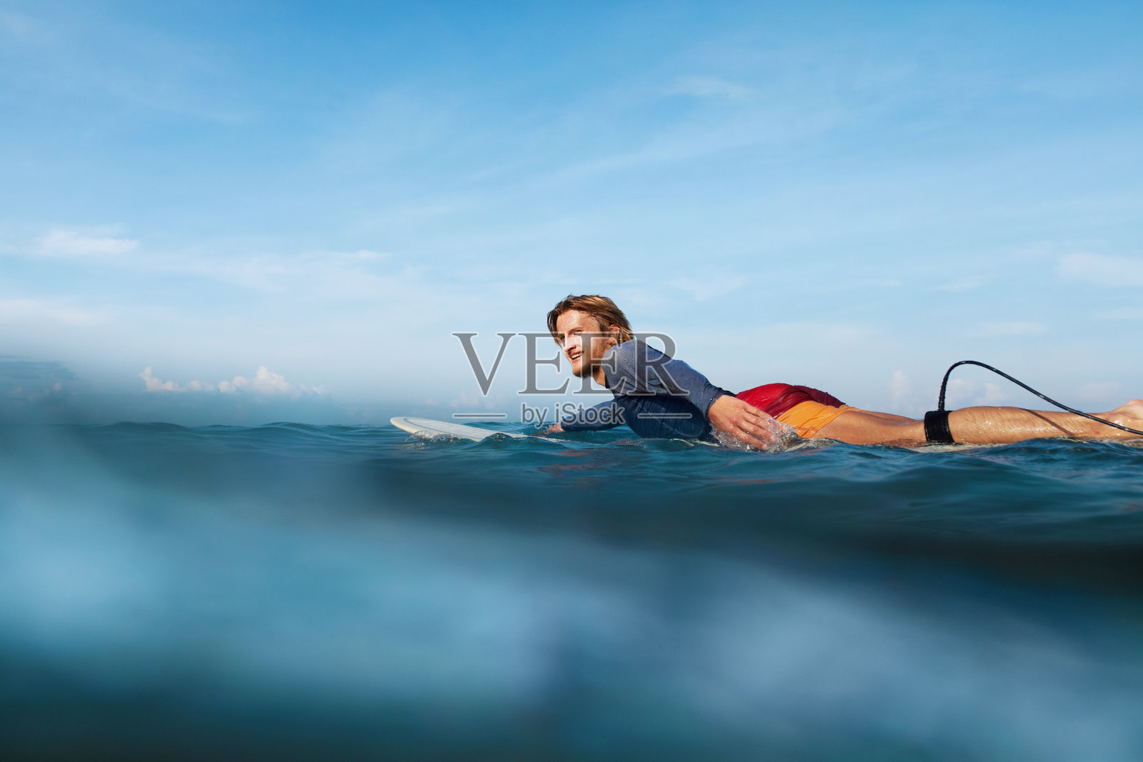 冲浪。冲浪板肖像上的冲浪者。穿着潜水服在海里游泳的帅哥。蓝绿色的海和蓝天的背景。照片摄影图片