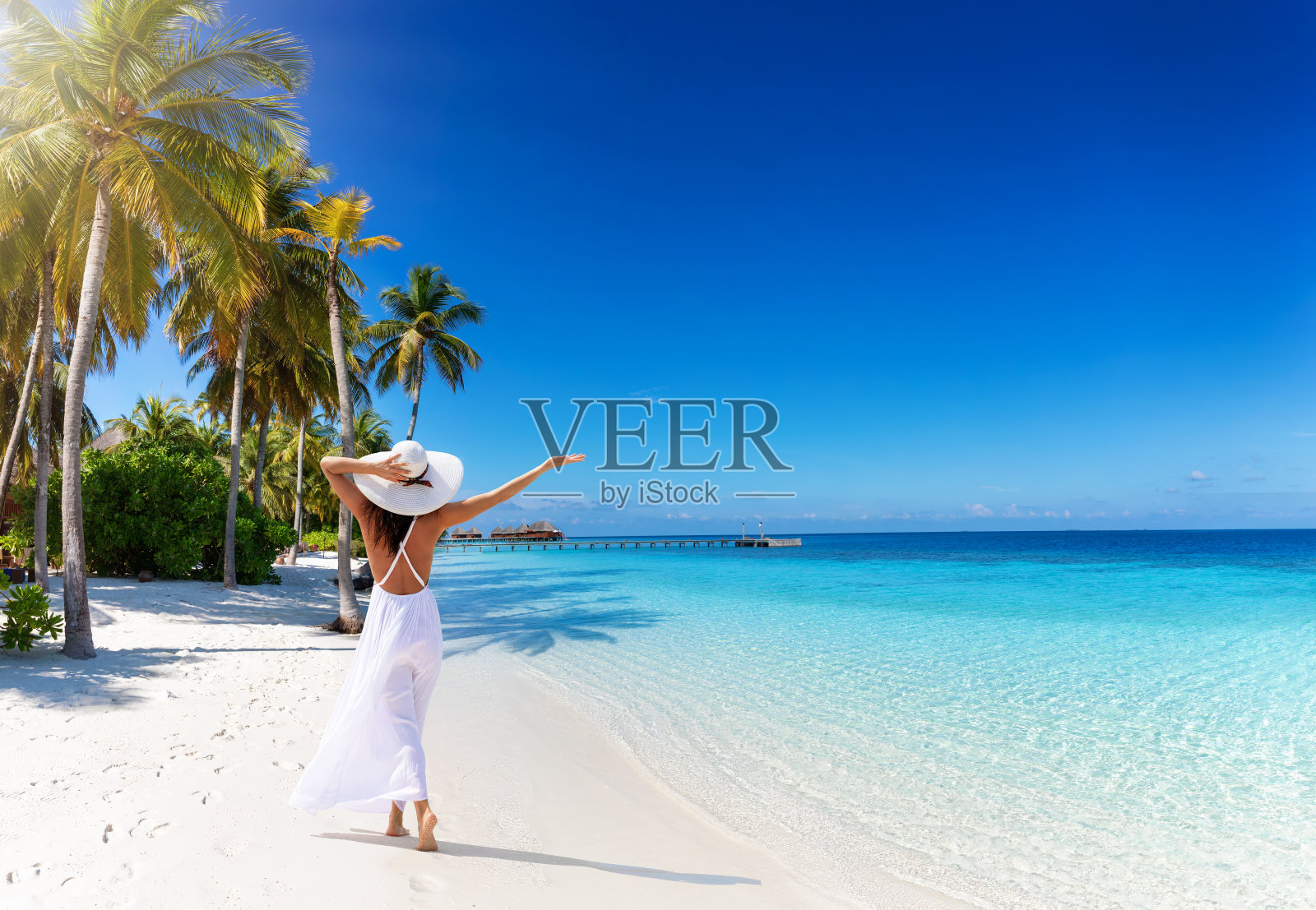 一位戴着白色帽子的女士走在棕榈树和绿松石海的热带天堂海滩上照片摄影图片