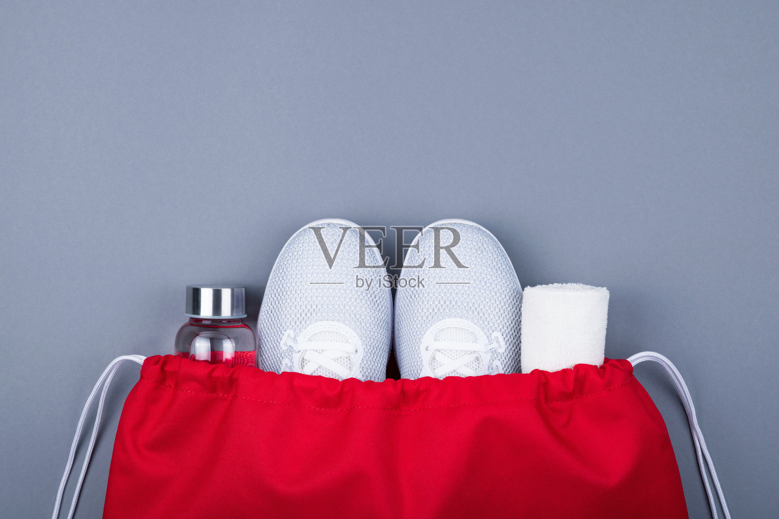 白色运动鞋，玻璃水瓶和毛巾在红色的运动包在灰色的背景。照片摄影图片