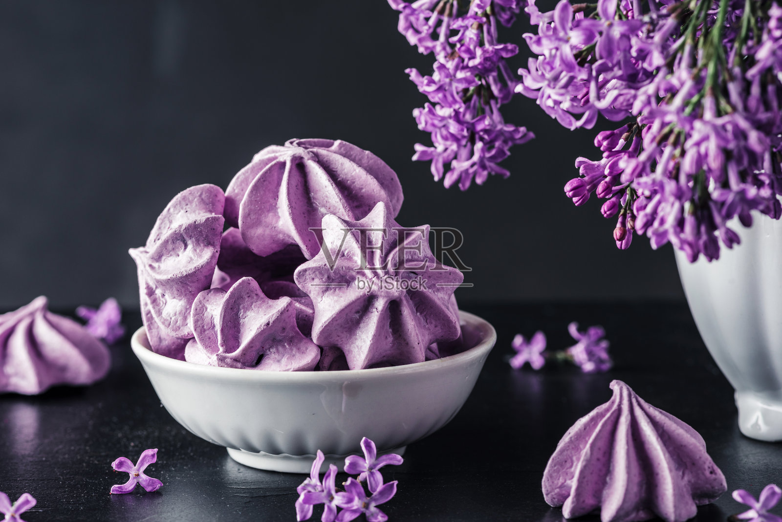 紫色的蛋白酥饼，在深底的花瓶上放着丁香花。低调。静物画照片摄影图片