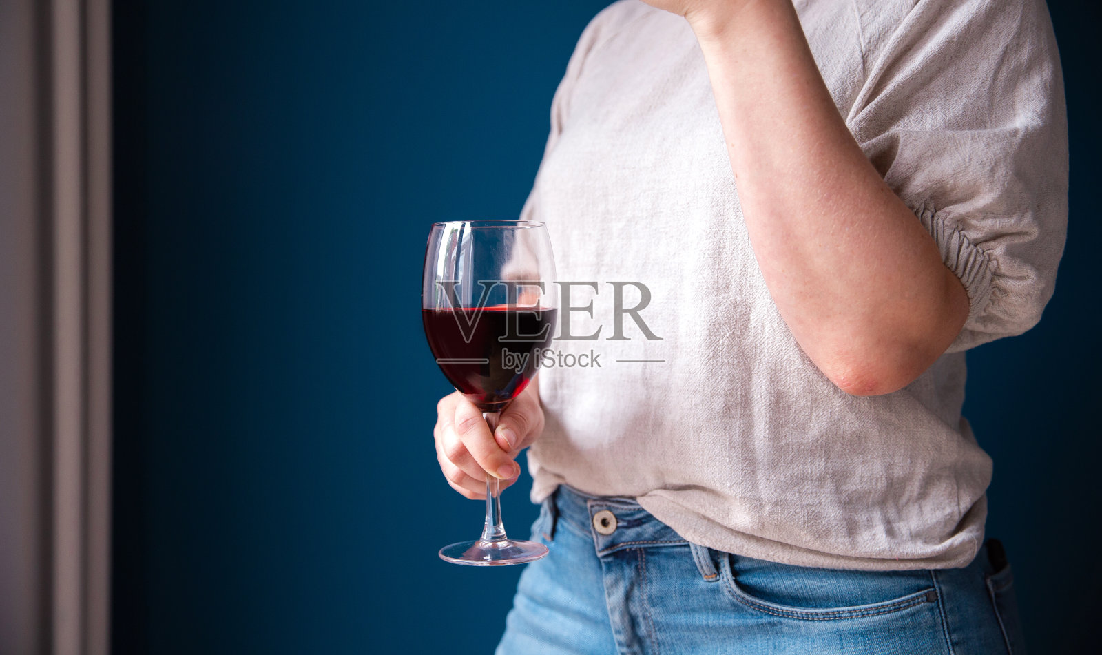 一幅年轻女子的肖像，手里拿着一杯红酒，靠在蓝色的墙上，照片摄影图片