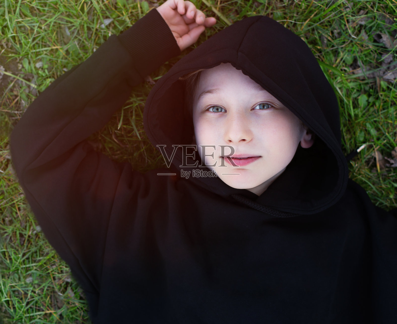笑着可爱的小男孩躺在绿色的草地上。从上面看照片摄影图片