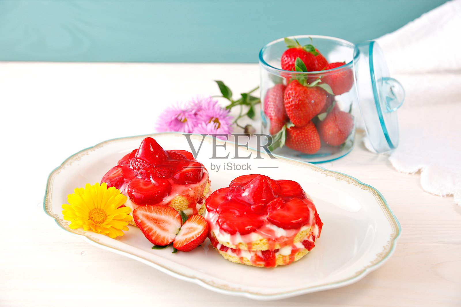 自制美味的迷你草莓酸奶奶油海绵蛋糕。新鲜草莓，绿色玻璃，桌布和花卉背景。甜草莓天然水果玻璃罐。照片摄影图片