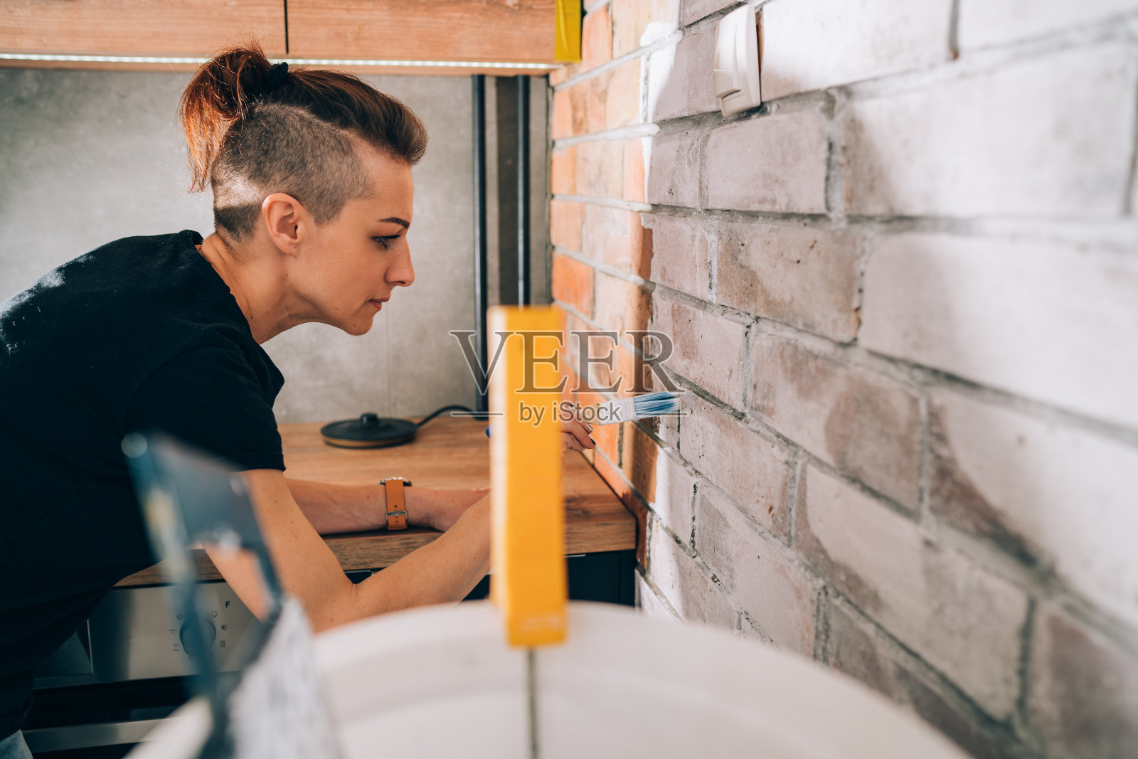 一名妇女正在装修厨房，将一堵砖墙刷成了白色照片摄影图片