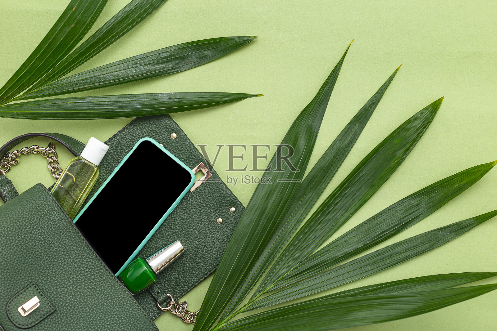 手提包，手机，指甲油和自然树叶在绿色的背景。单色。本空间照片摄影图片