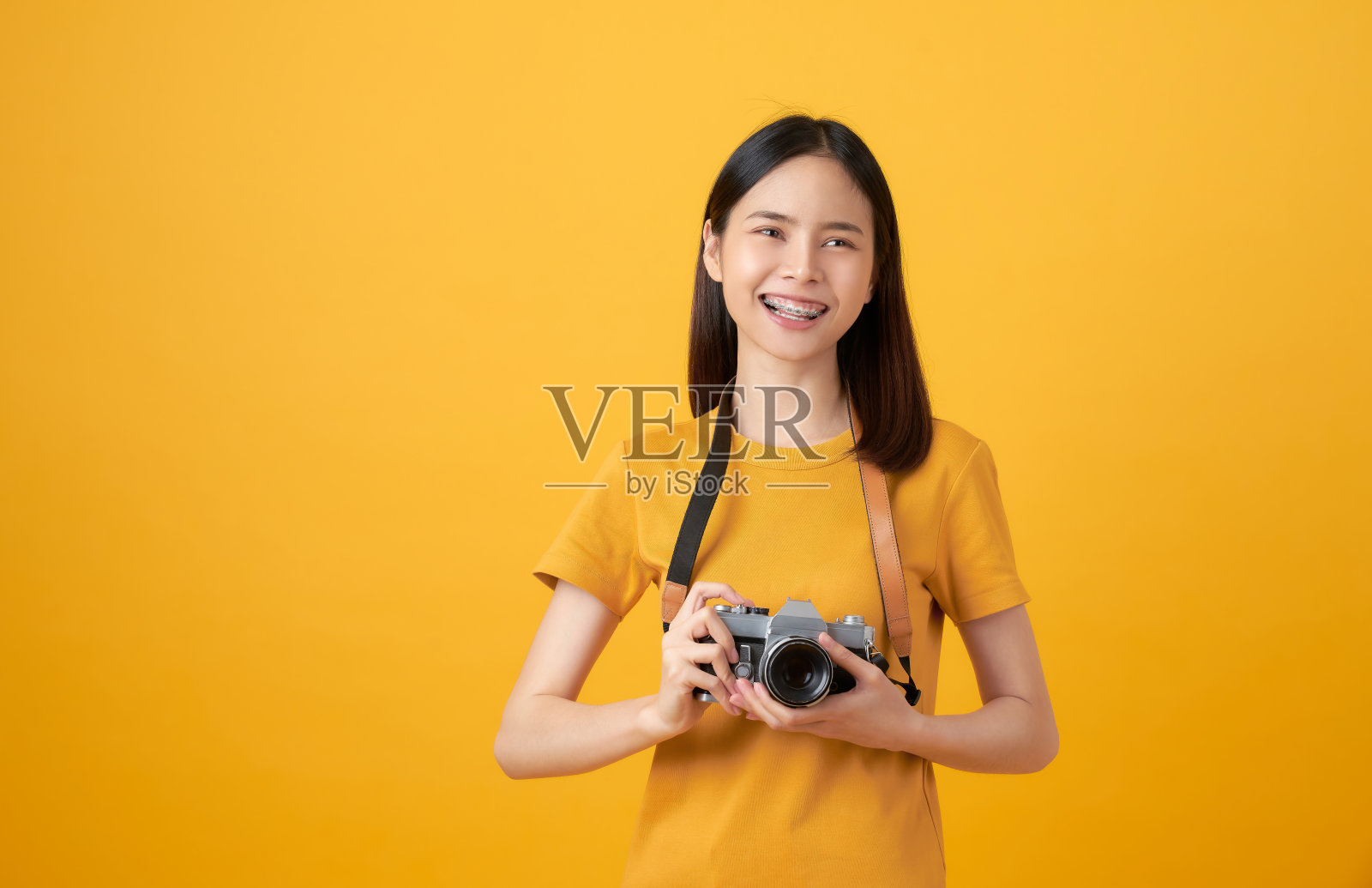 年轻微笑的亚洲女性游客拿着相机，寻找复制的空间上的黄色背景。照片摄影图片