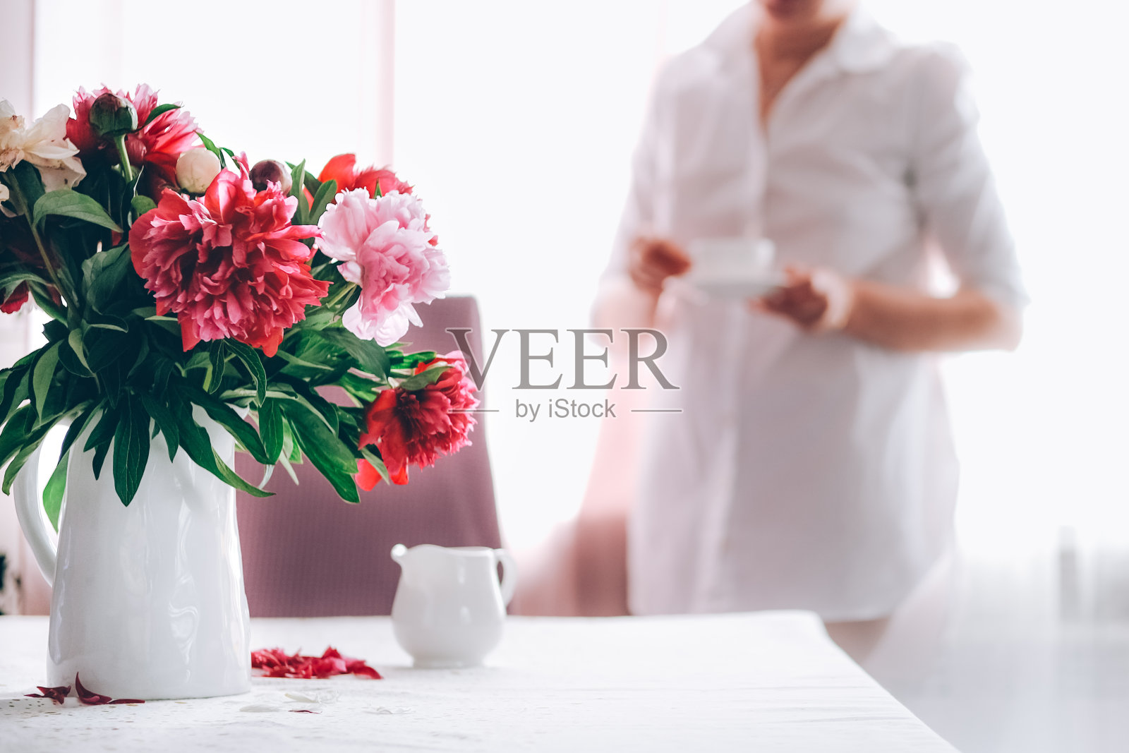 一个女人在用粉色牡丹装饰的厨房里喝着咖啡。照片摄影图片
