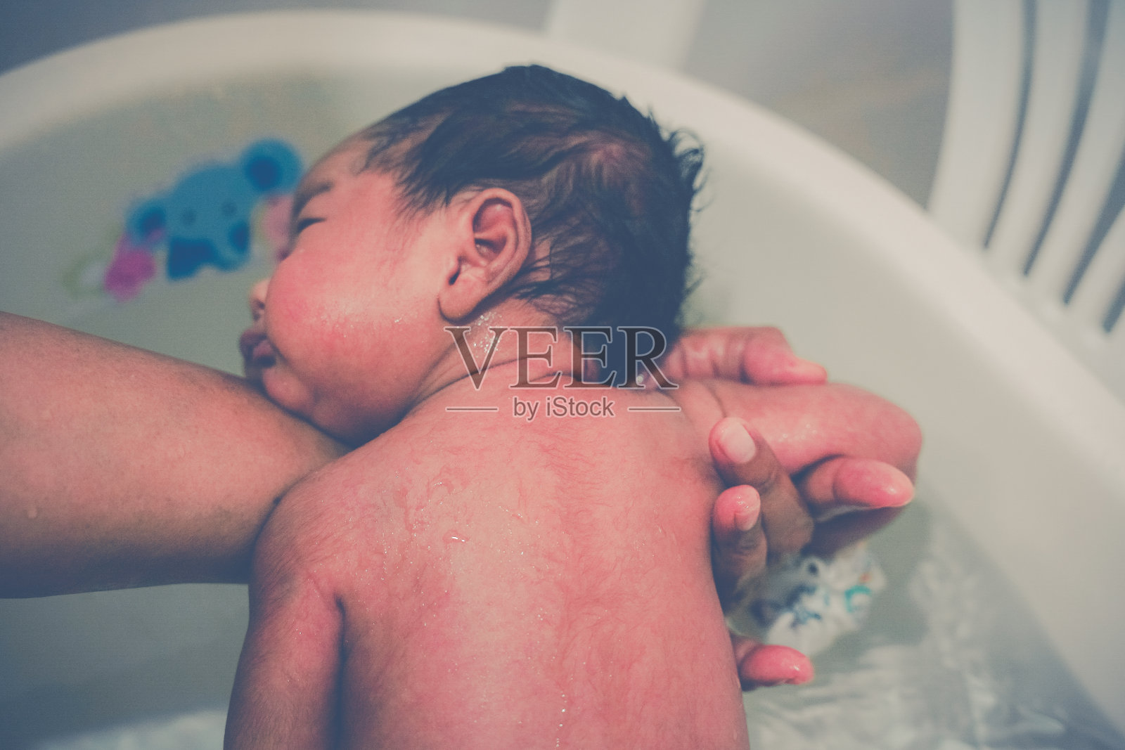 一位母亲正在浴室的塑料盆里为新生儿洗澡和洗漱。照片摄影图片