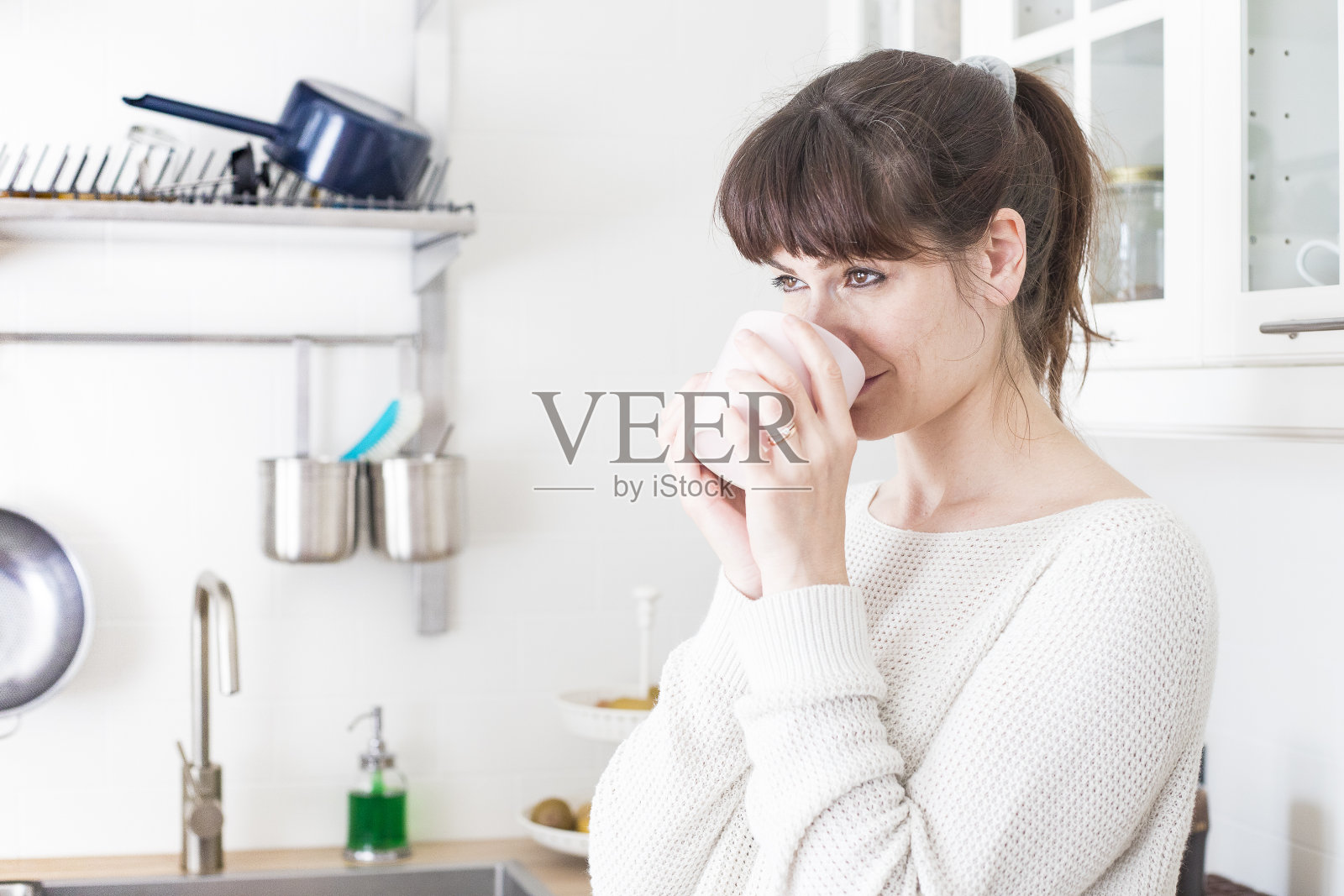 女人在白色的厨房里喝着水，面带微笑。积极的氛围。照片摄影图片