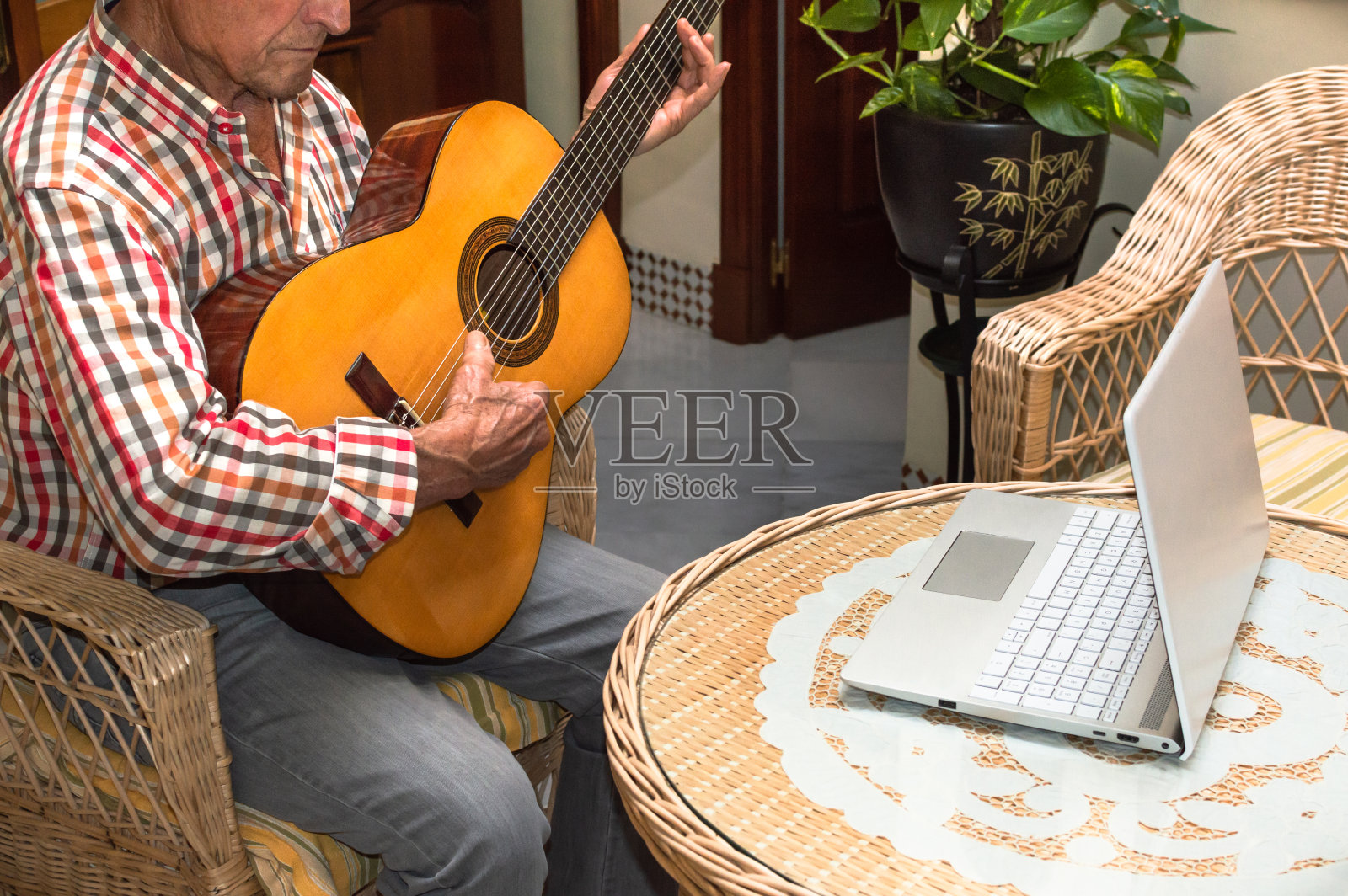 一位老人在家里用电脑学习弹吉他。老人与技术，远程课程或在线教程的概念。照片摄影图片