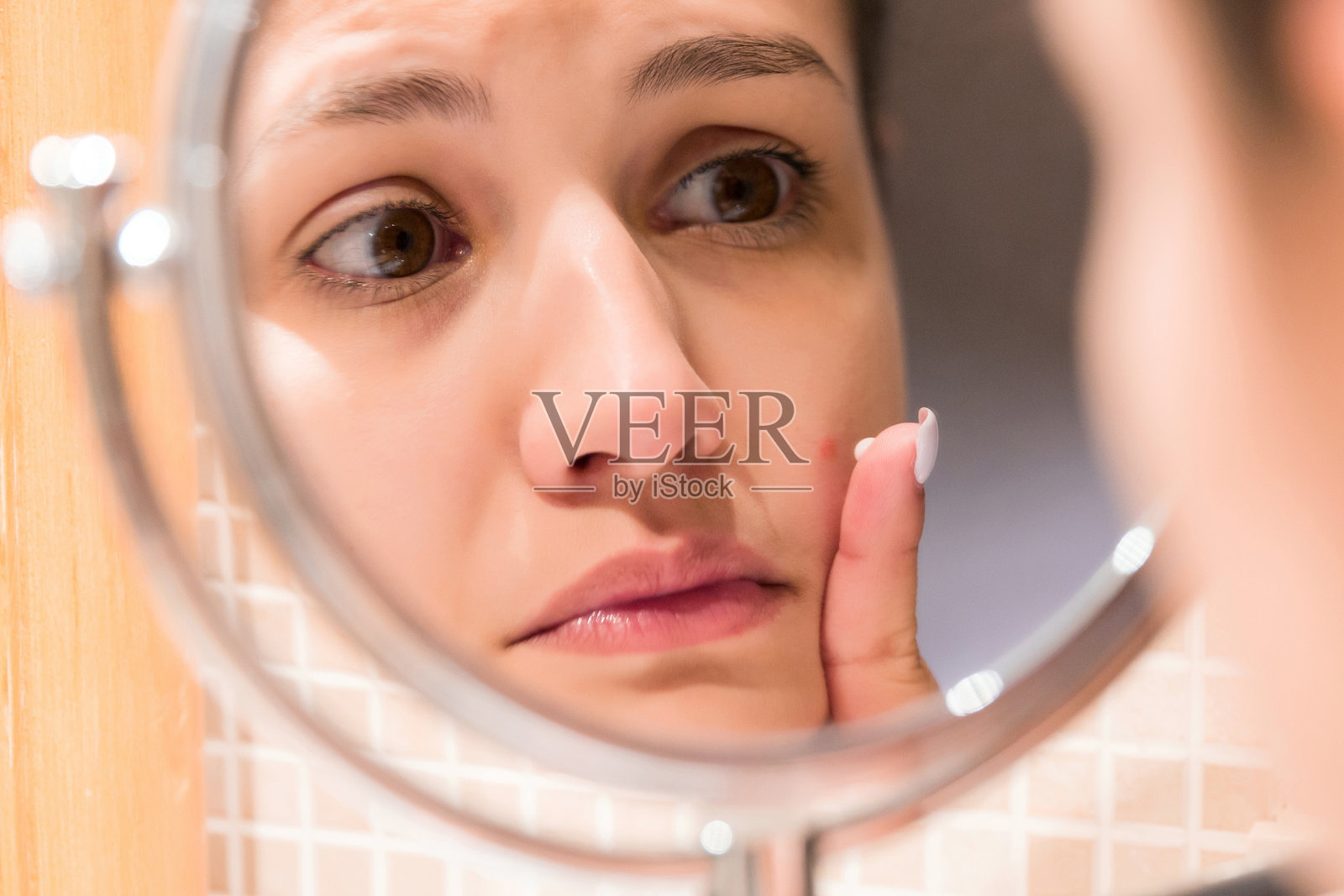 一个小女孩在浴室镜子前给一个红痘痘涂霜。美容、护肤和健康的早晨概念照片摄影图片