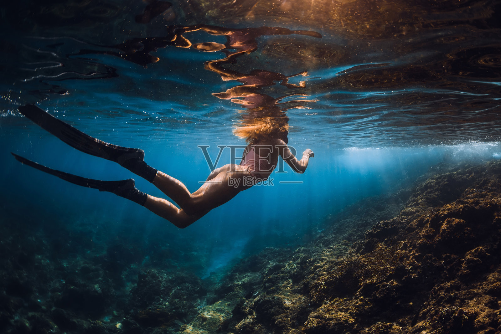 年轻的自由潜水女子有鳍和迷人的阳光滑行。在水下自由潜水照片摄影图片