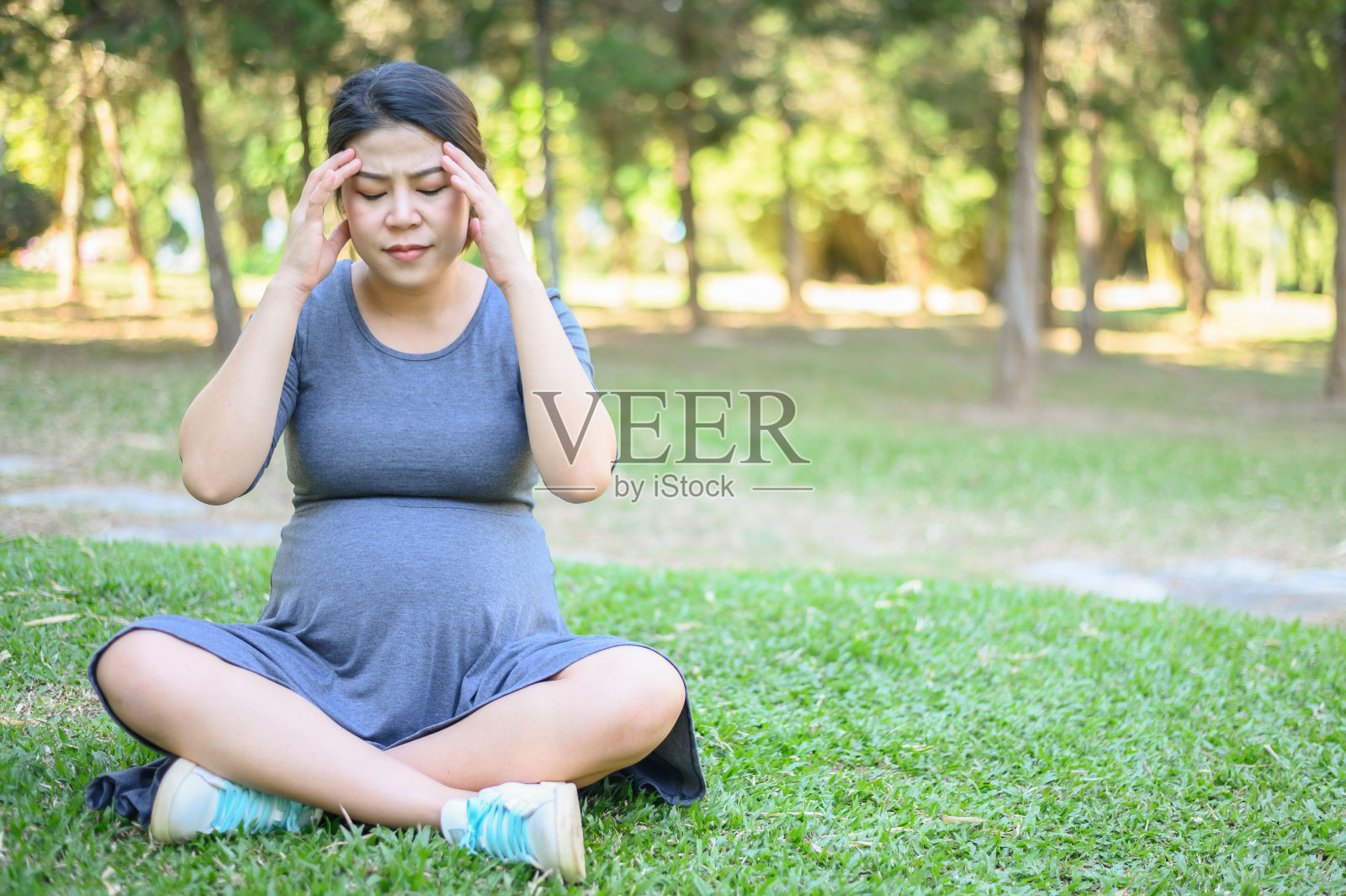 一名孕妇坐在公园里感到头痛和头晕。照片摄影图片