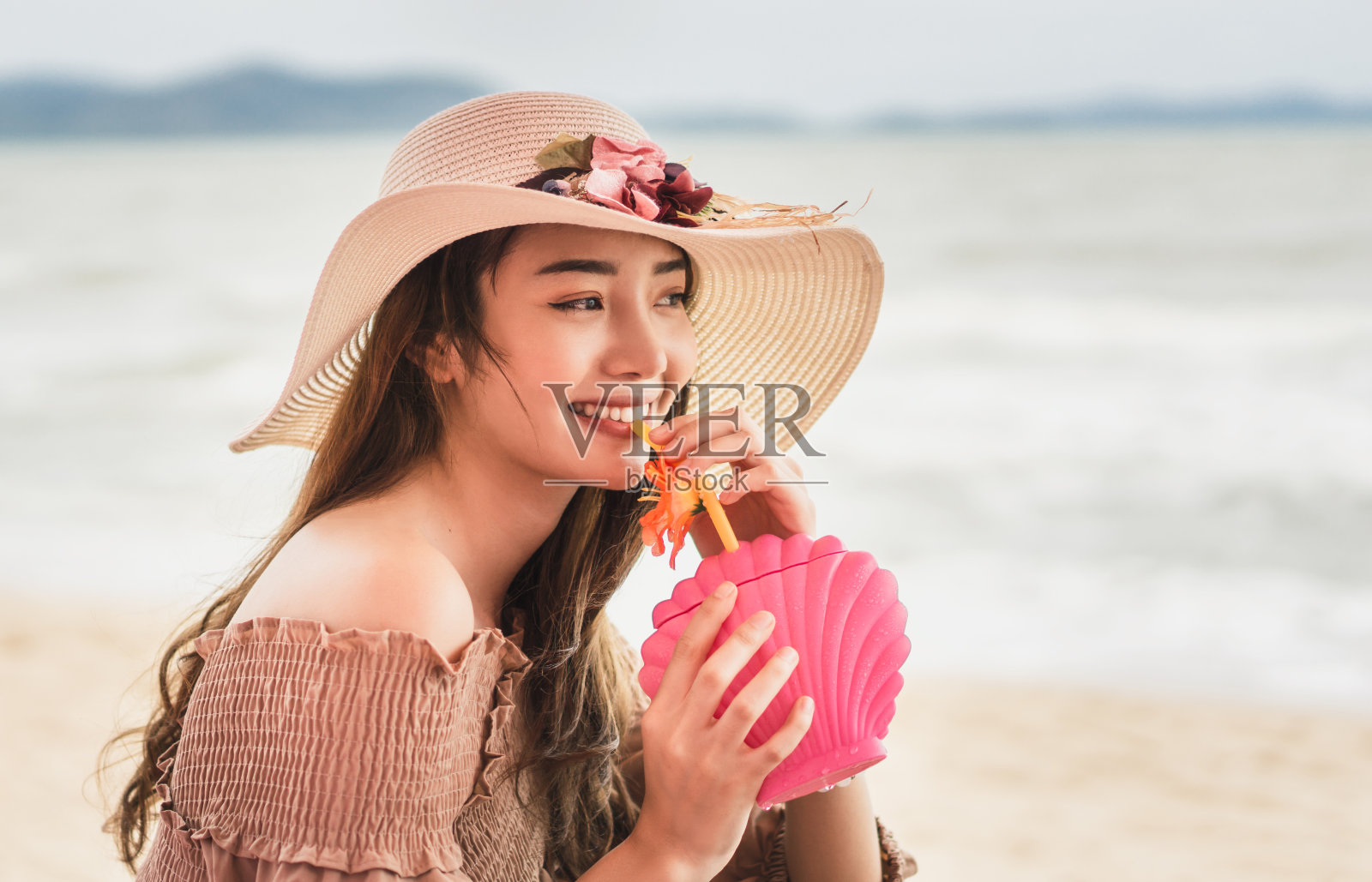 在海滩上喝鸡尾酒的亚洲女人。照片摄影图片
