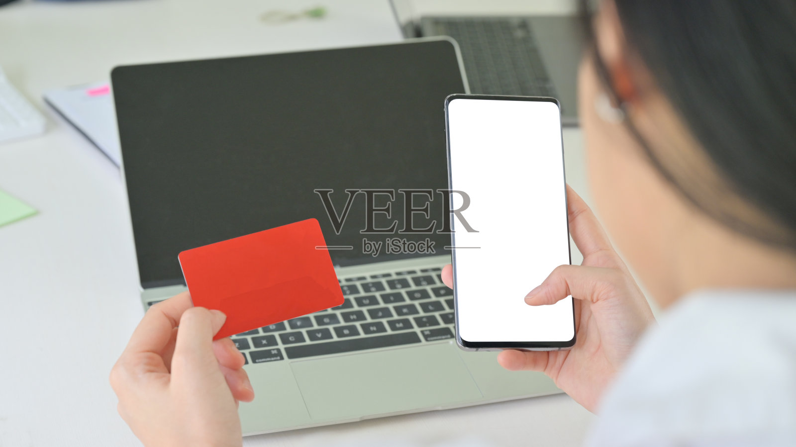 女人手里拿着信用卡和智能手机，后面放着笔记本电脑。照片摄影图片