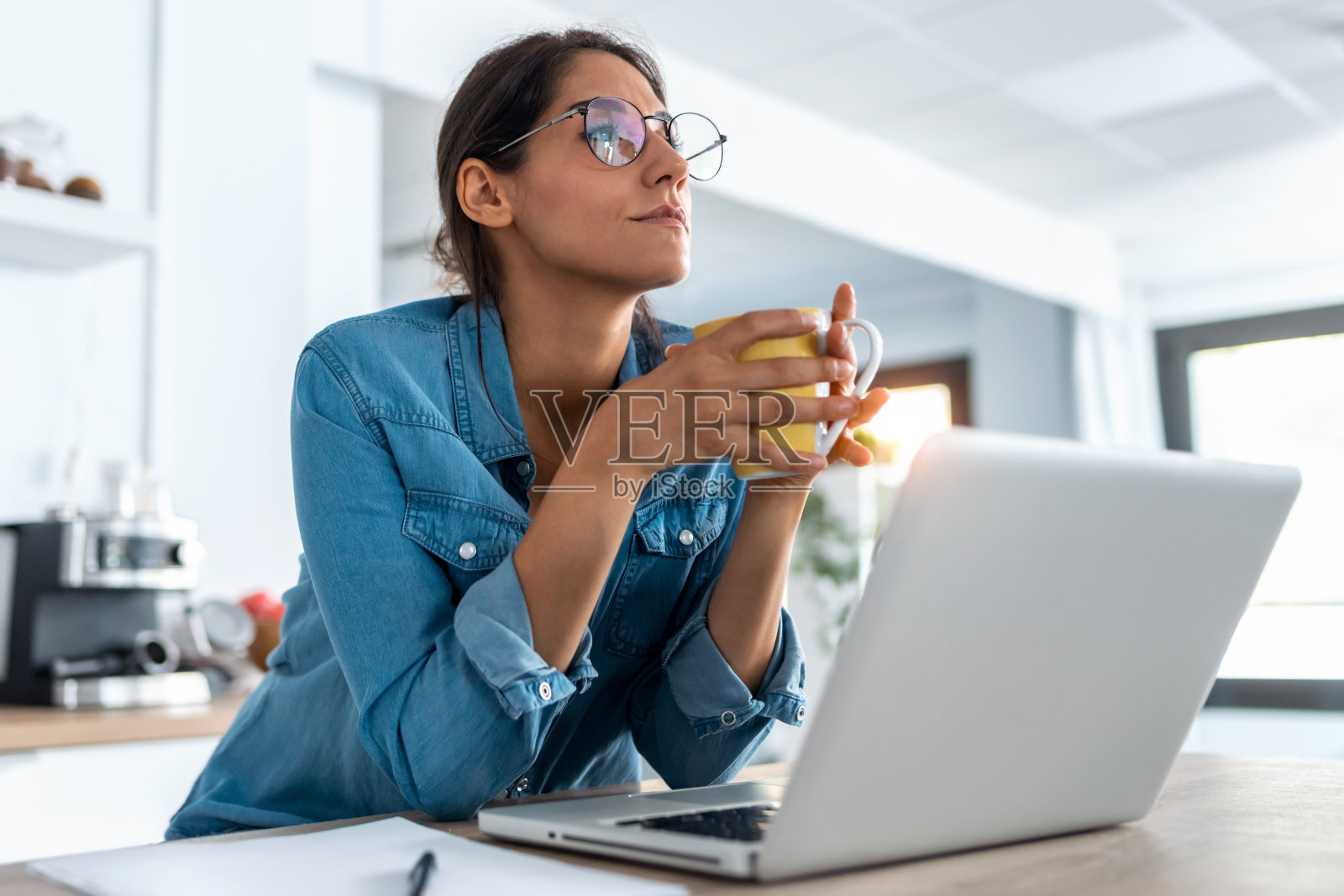 年轻漂亮的女人放松了一会儿，喝着咖啡，在厨房里用笔记本电脑工作。照片摄影图片