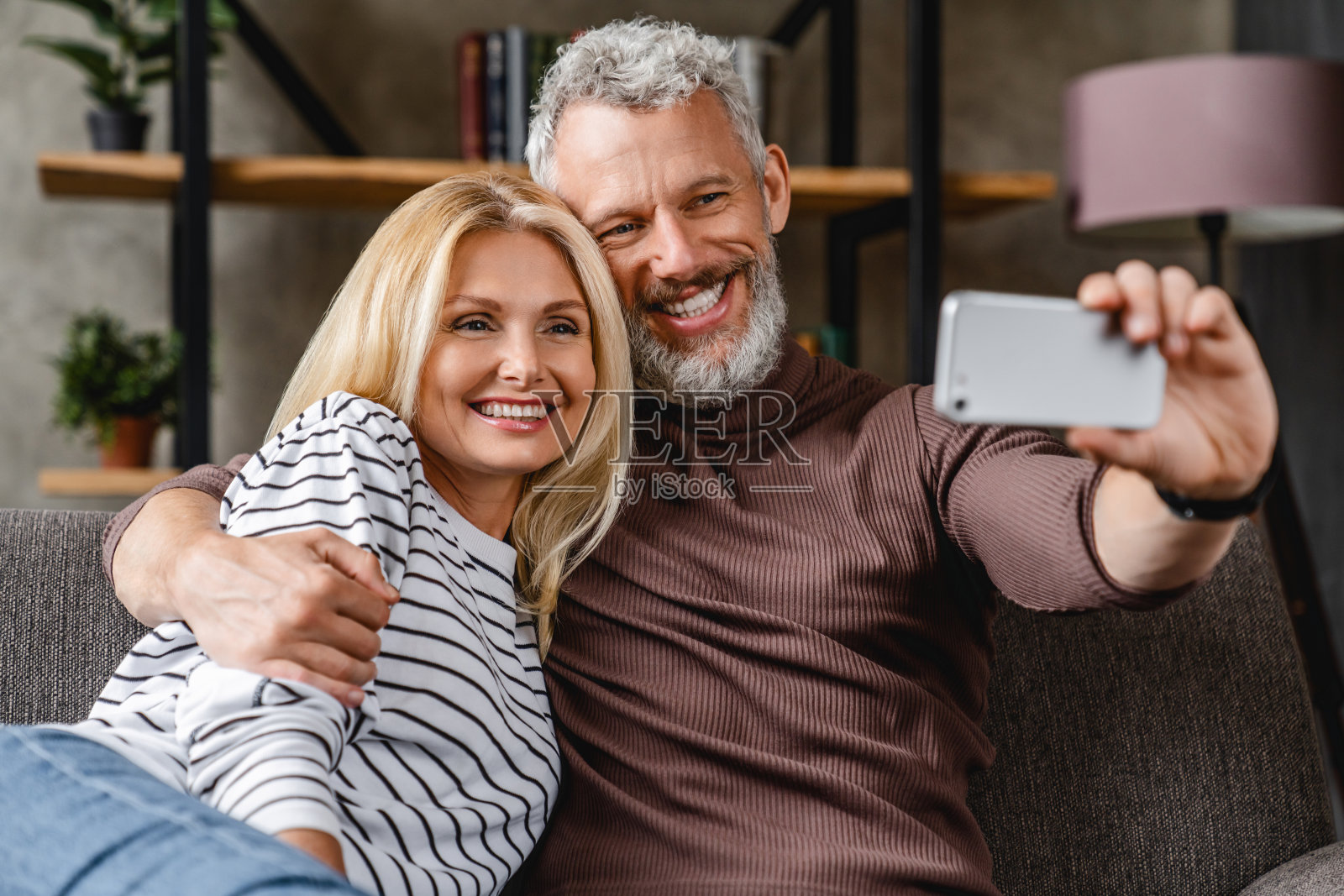 现代中年夫妇坐在家里的沙发上，用智能手机自拍照片摄影图片