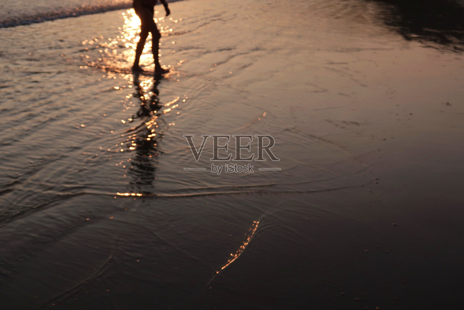 在印度南部喀拉拉邦的果阿/喀拉拉邦，一个年轻的印度人走到远处，沿着热带Palolem海滩的日落海滩，穿着t恤，短裤，拿着人字拖凉鞋的鞋子从后面看照片摄影图片