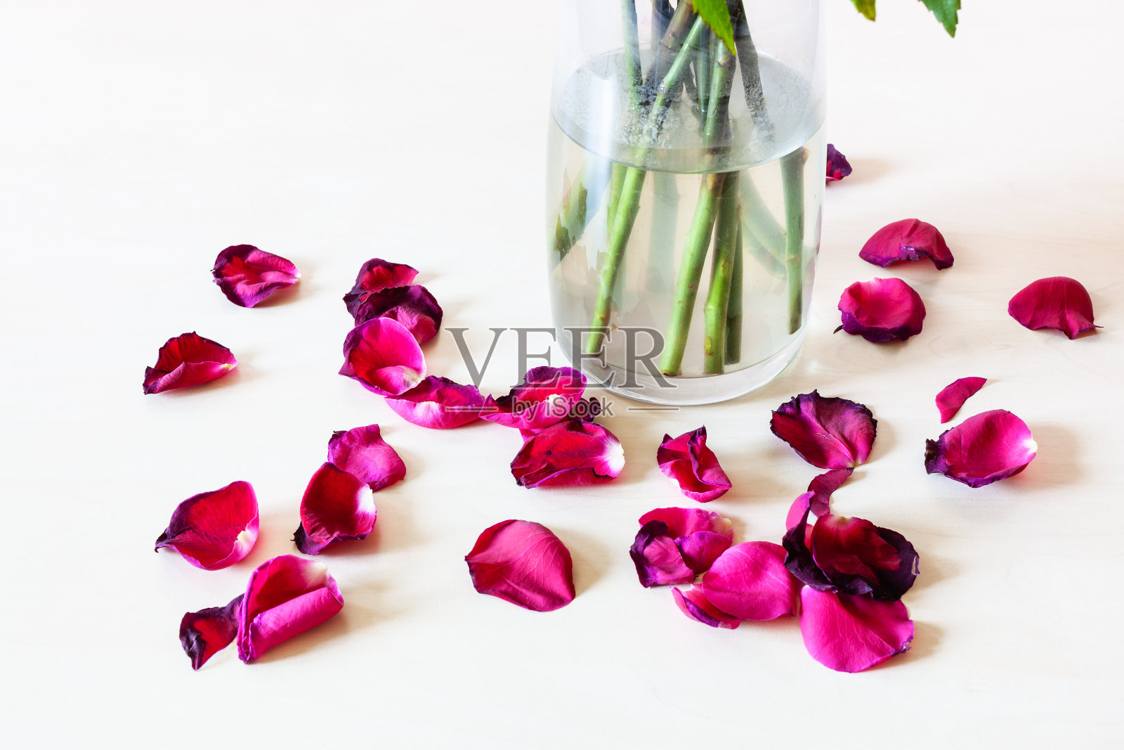 玻璃花瓶旁散落的红玫瑰花瓣照片摄影图片
