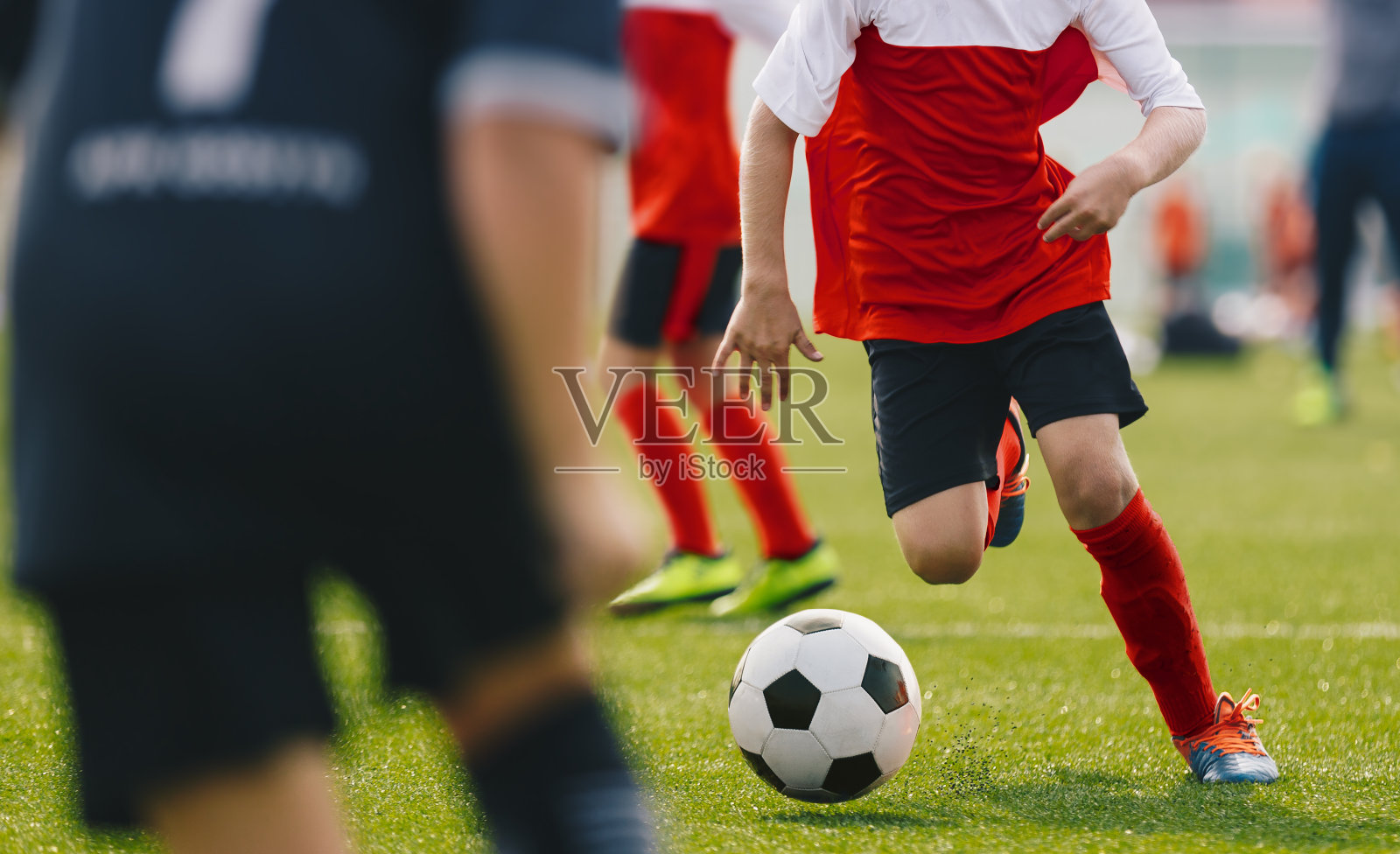 足球运动员运球，年轻的足球运动员在带球跑。男孩踢运动足球比赛在阳光明媚的夏天。青少年足球比赛照片摄影图片