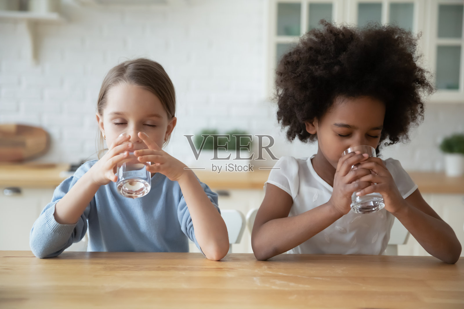 两个多民族小女孩坐在厨房里喝着天然水照片摄影图片