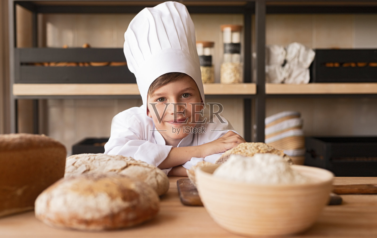 快乐的小面包师倚在桌子上照片摄影图片