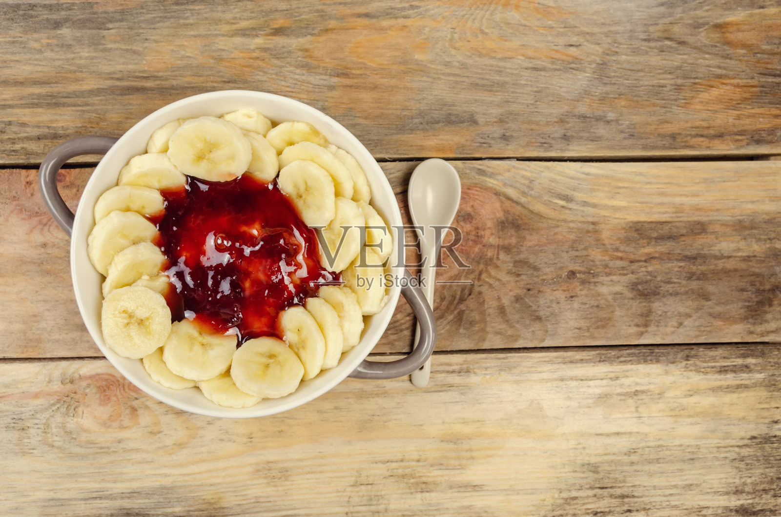 白灰色的盘子里有果酱和香蕉，白色的勺子，木质的背景，俯视图，拷贝空间。健康的早餐。照片摄影图片