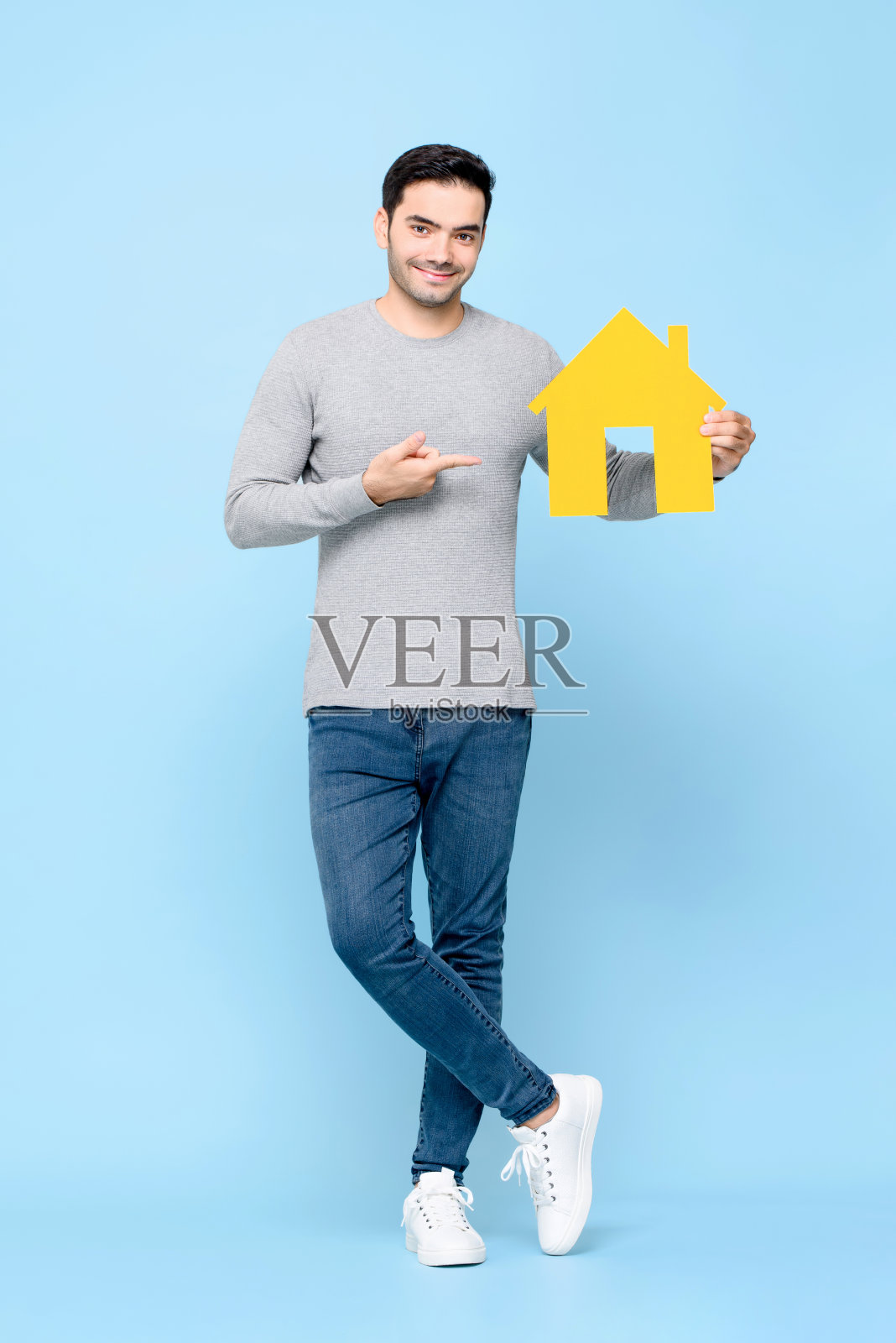 英俊微笑的白人男子站着，指着黄色的房子模型照片摄影图片