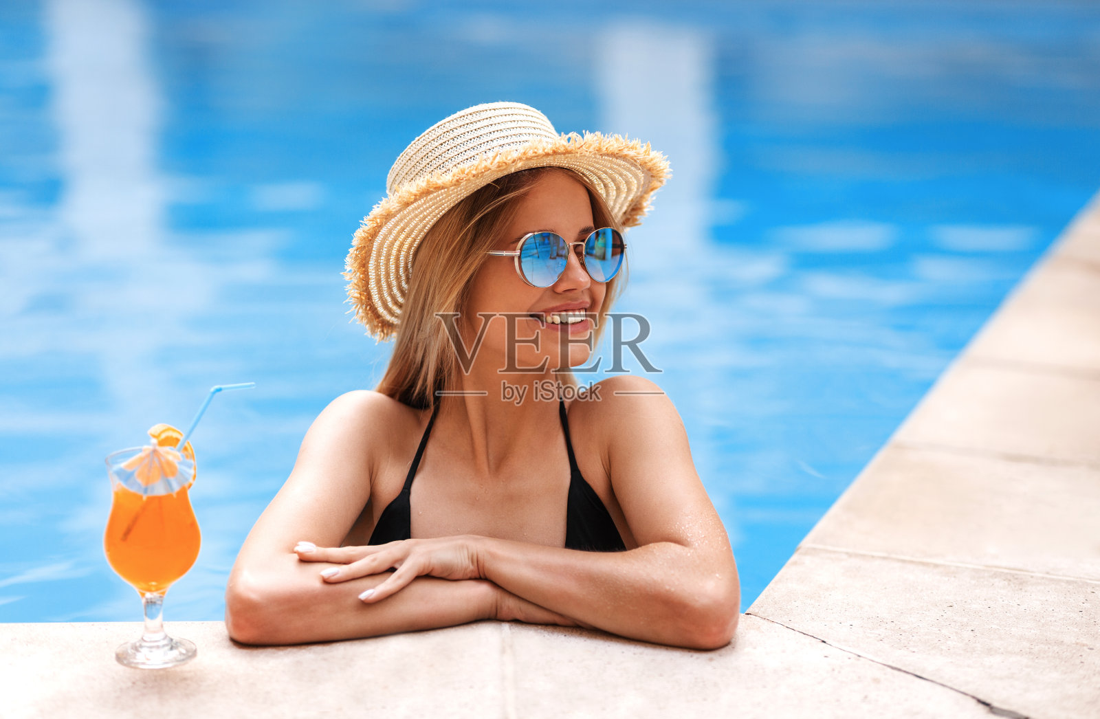 快乐的金发女孩喝着鸡尾酒放松在泳池边，空白的空间照片摄影图片
