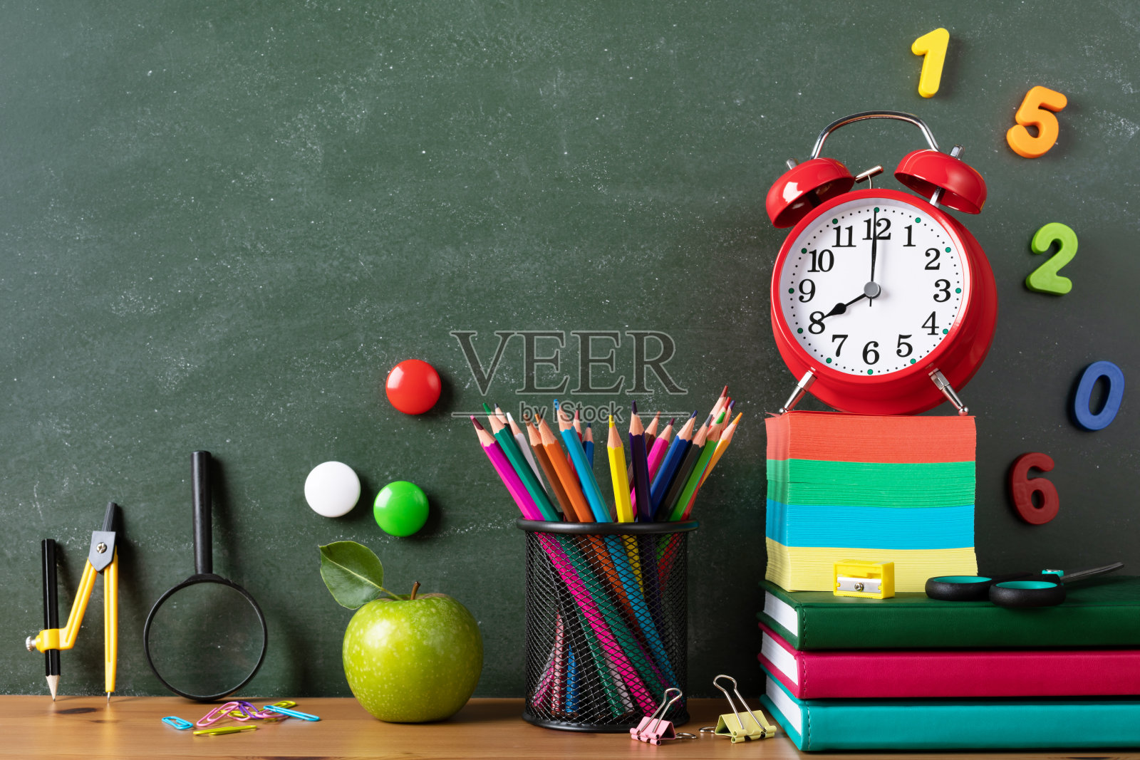 回到学校或教育理念，用闹钟、青苹果和学习用品贴在黑板上的木桌上。照片摄影图片