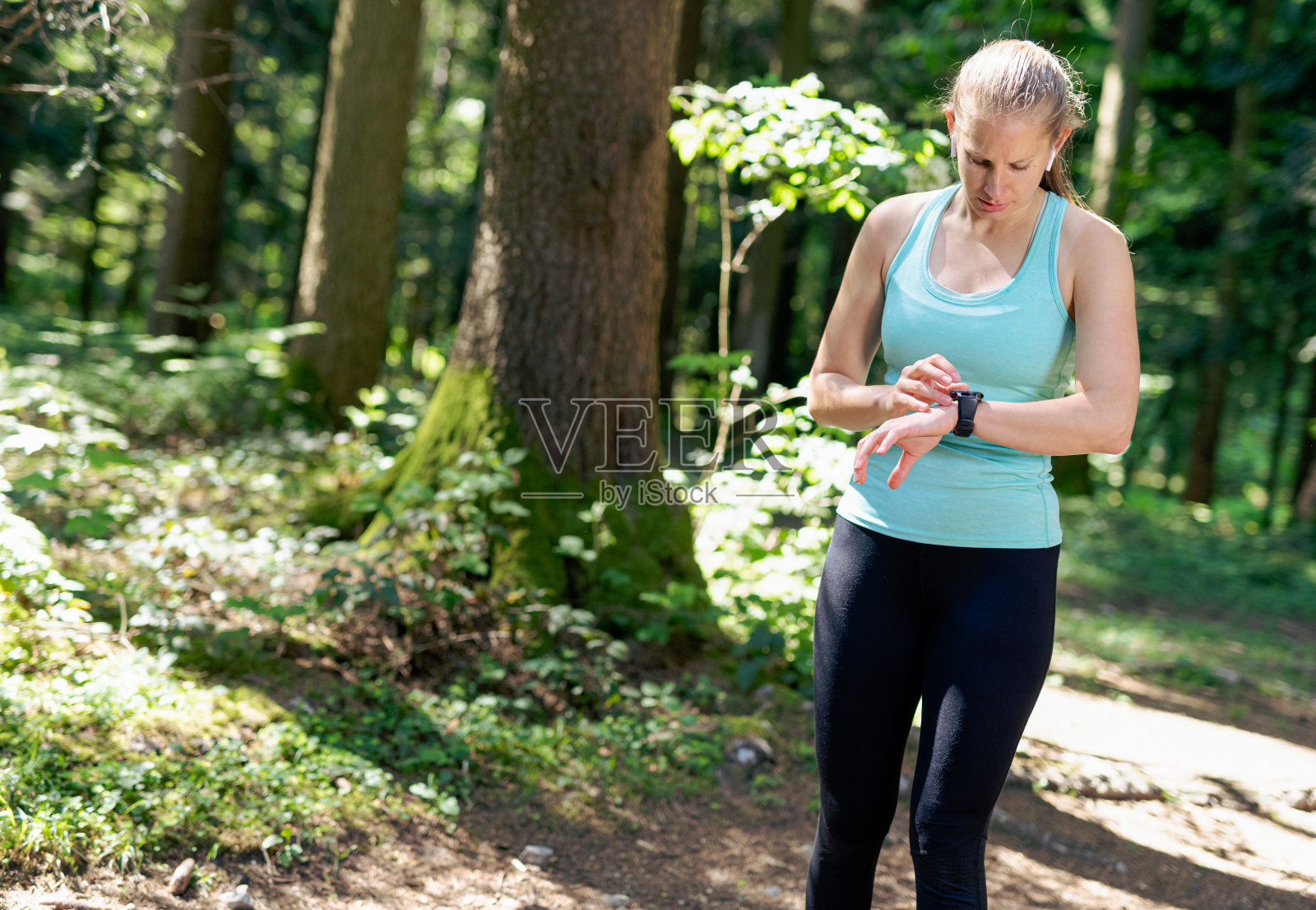 在树林里跑步的女人在看智能手表照片摄影图片