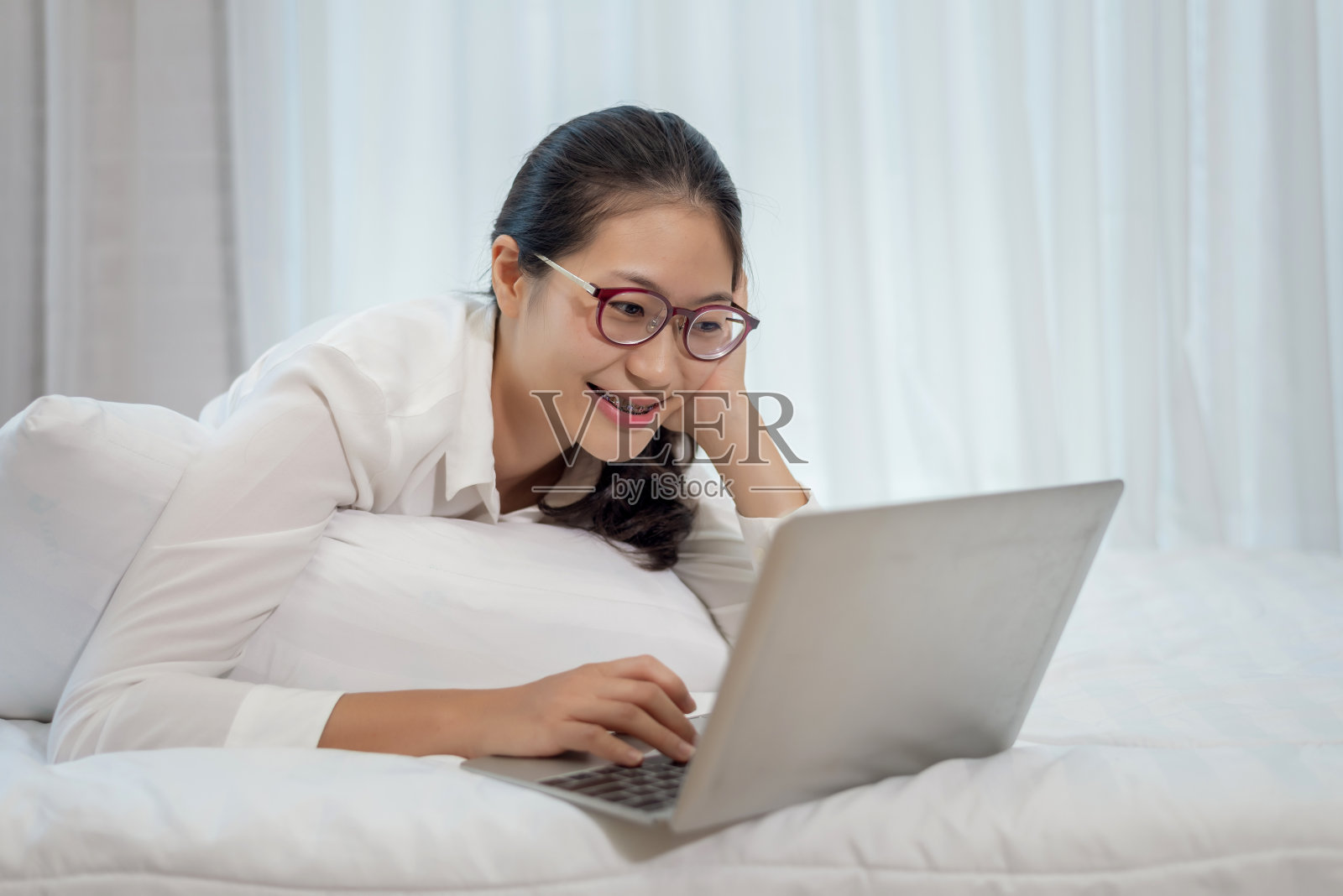年轻的亚洲女性在家里的床上用笔记本电脑工作。照片摄影图片