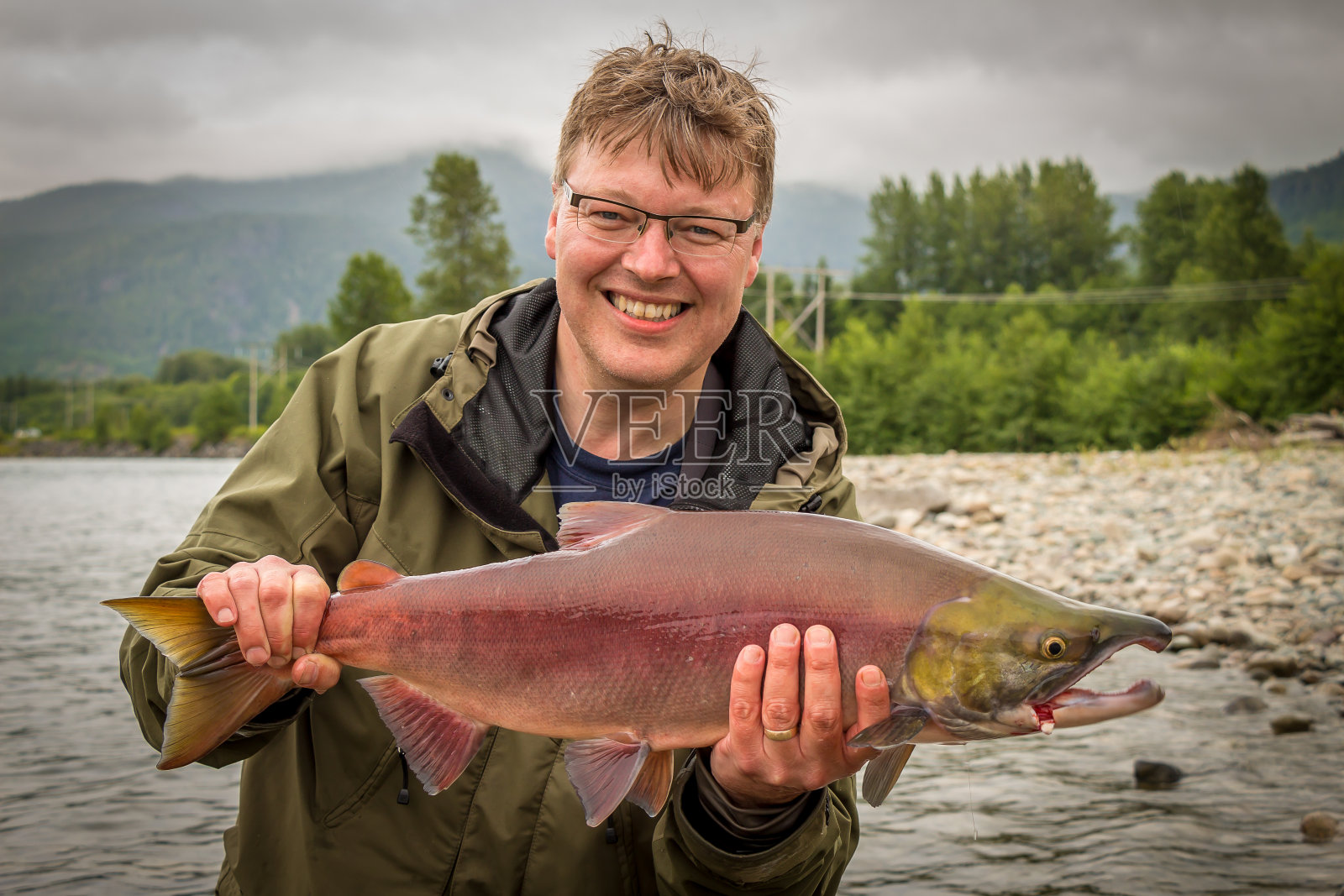 一个快乐的渔夫骄傲地举起一只红鲑鱼照片摄影图片
