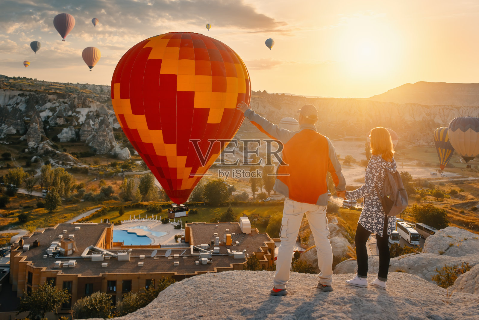 在土耳其卡帕多西亚，一对游客在一个阳光明媚的清晨观看彩色气球飞行。照片摄影图片