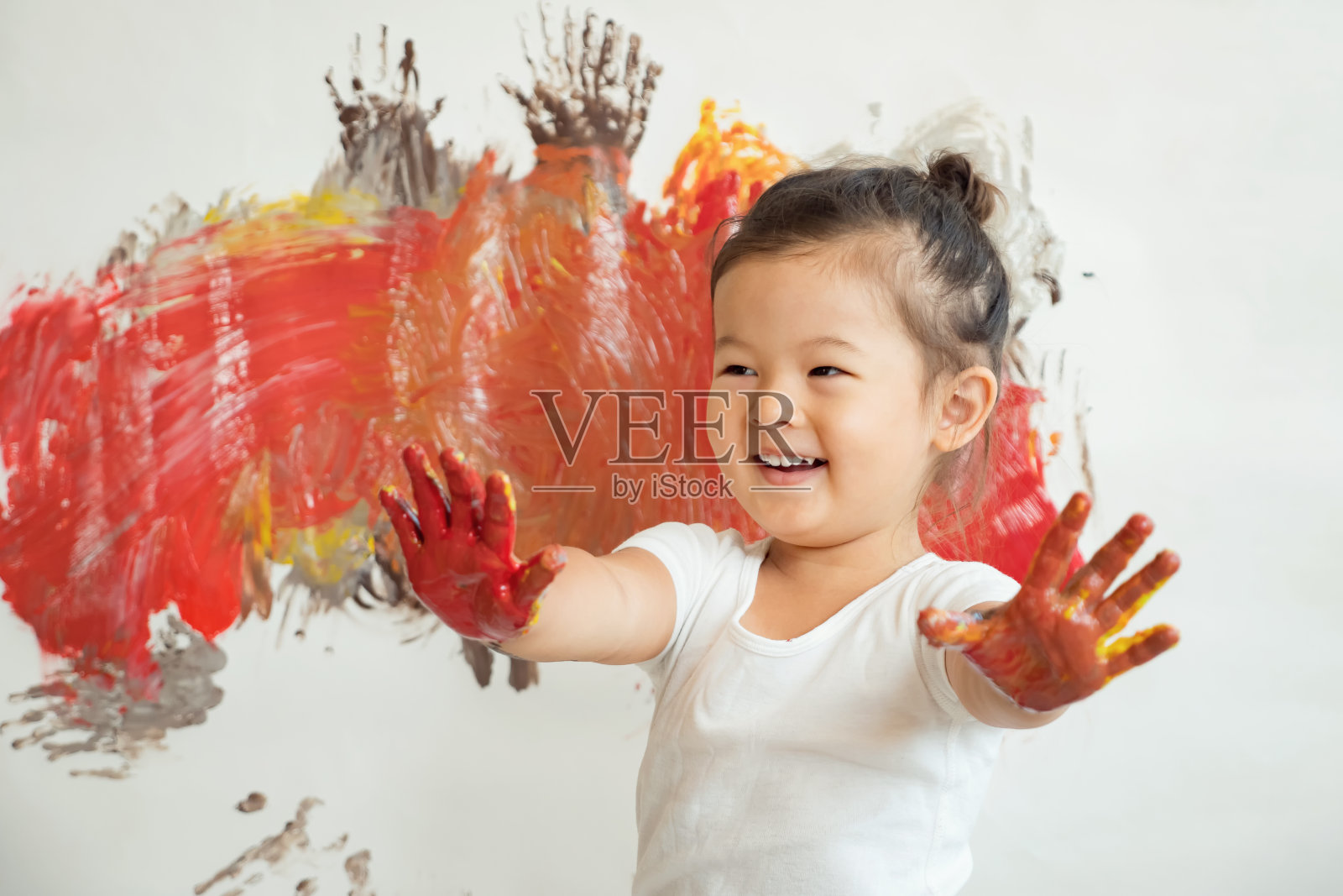 这个美丽的亚洲女孩穿着白色t恤，双手涂满颜料，面带微笑，背景是一堵油漆墙照片摄影图片
