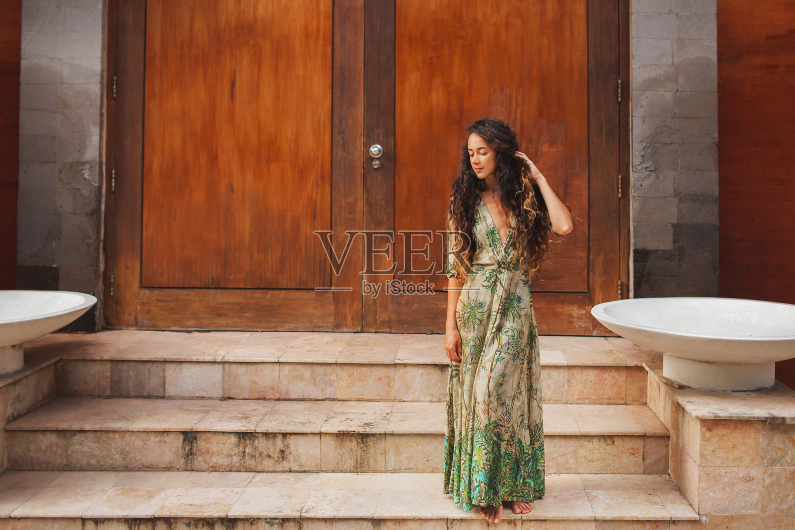在木门的背景上，一个穿着绿色丝绸衣服的深色卷发女人的肖像。亚洲风格和建筑。照片摄影图片