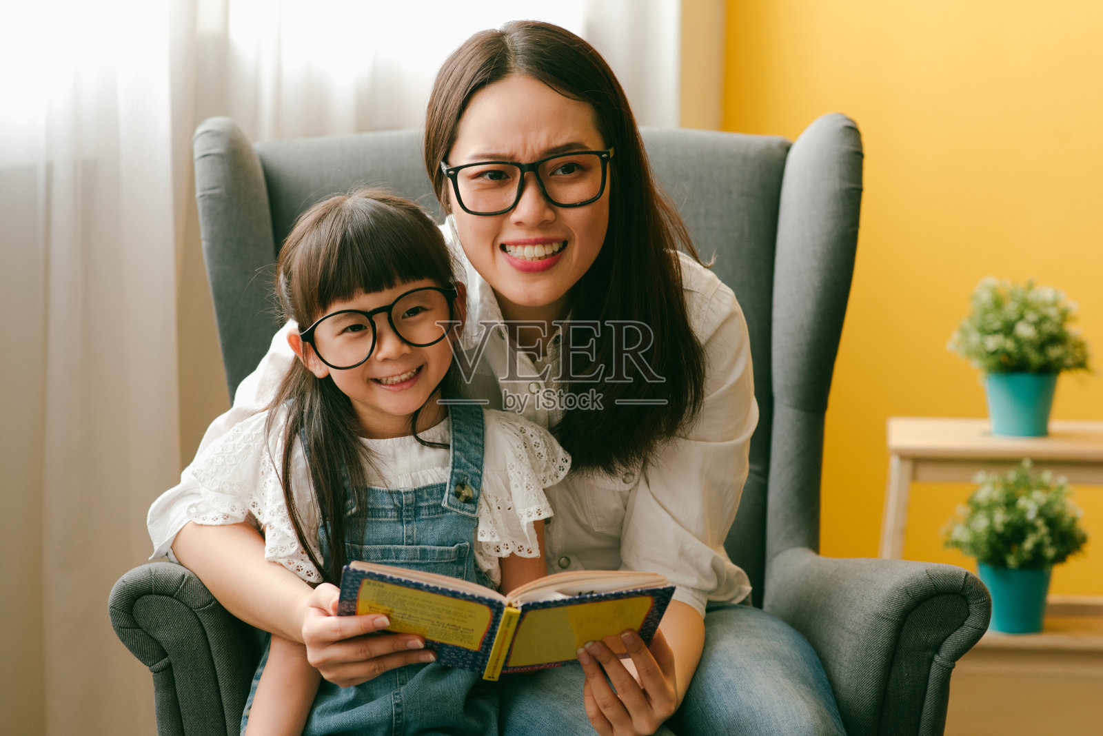 亚洲母亲和女儿在客厅读故事书。照片摄影图片