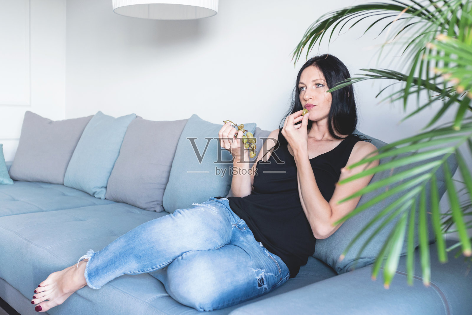 一个女人坐在家里的沙发上吃葡萄照片摄影图片