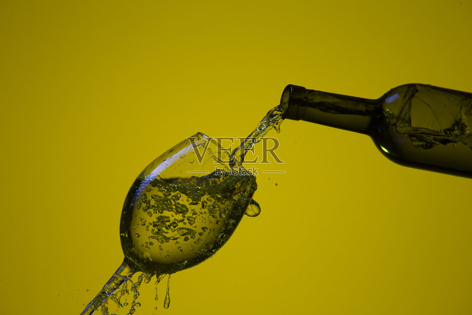 饮料倒出的瓶子在右手边的葡萄酒杯与彩色液体和水滴。水平的形象定位照片摄影图片