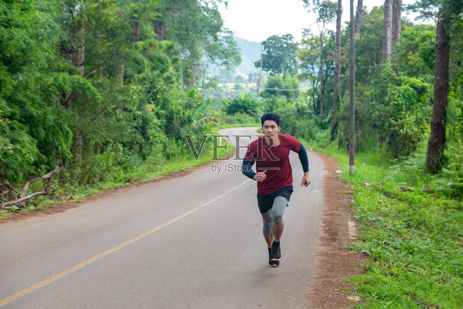 健康英俊的亚洲男子穿着运动服在夏季的山路上跑步。强壮的男运动员喜欢在草山上慢跑。户外运动的生活方式和极限运动训练的概念。照片摄影图片