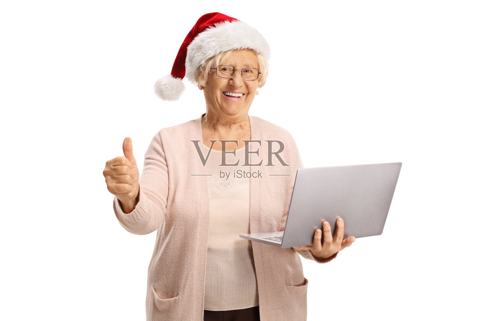 一个快乐的老妇人拿着一台笔记本电脑，戴着圣诞老人的帽子，竖起大拇指照片摄影图片