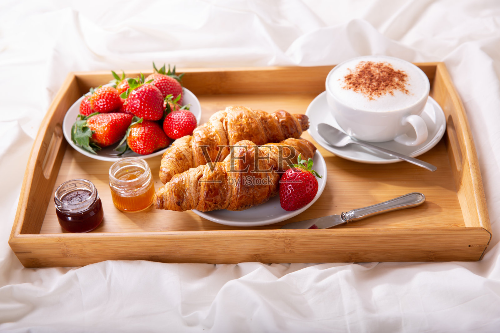 早餐托盘放在床上:一杯卡布奇诺和羊角面包照片摄影图片