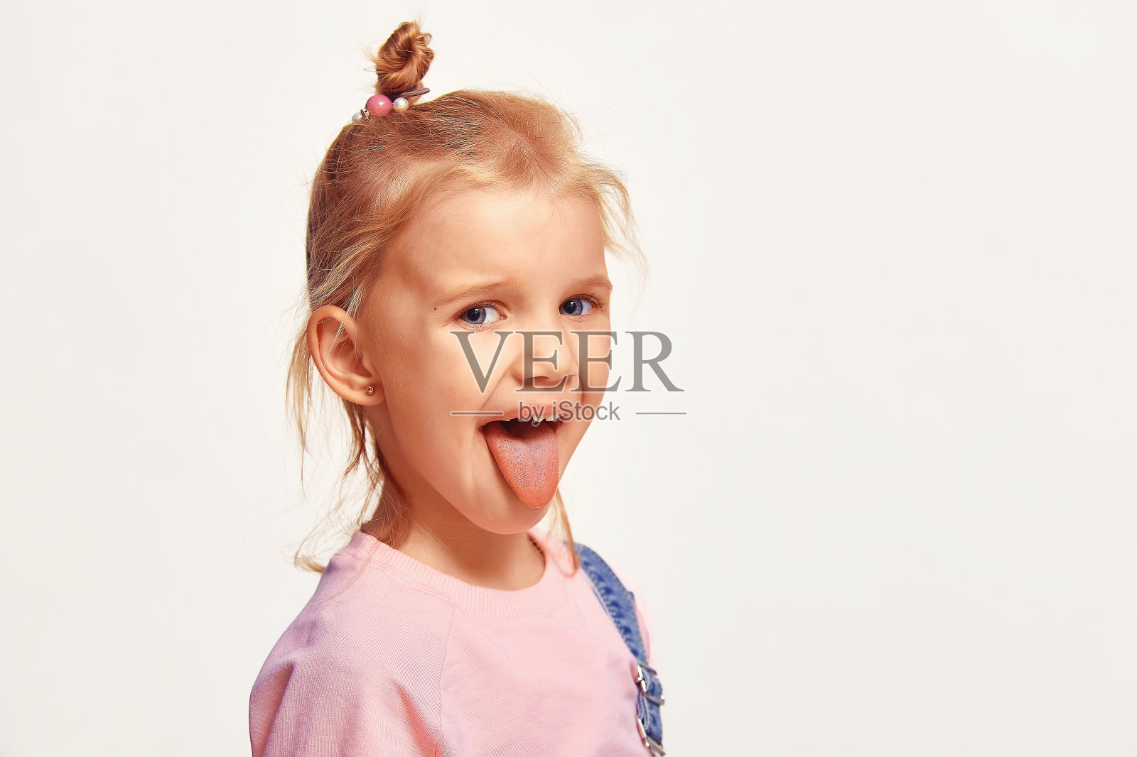 4-5岁的小女孩微笑着露出舌头。白种可爱的小孩穿着粉红色的运动衫，白色的背景照片摄影图片